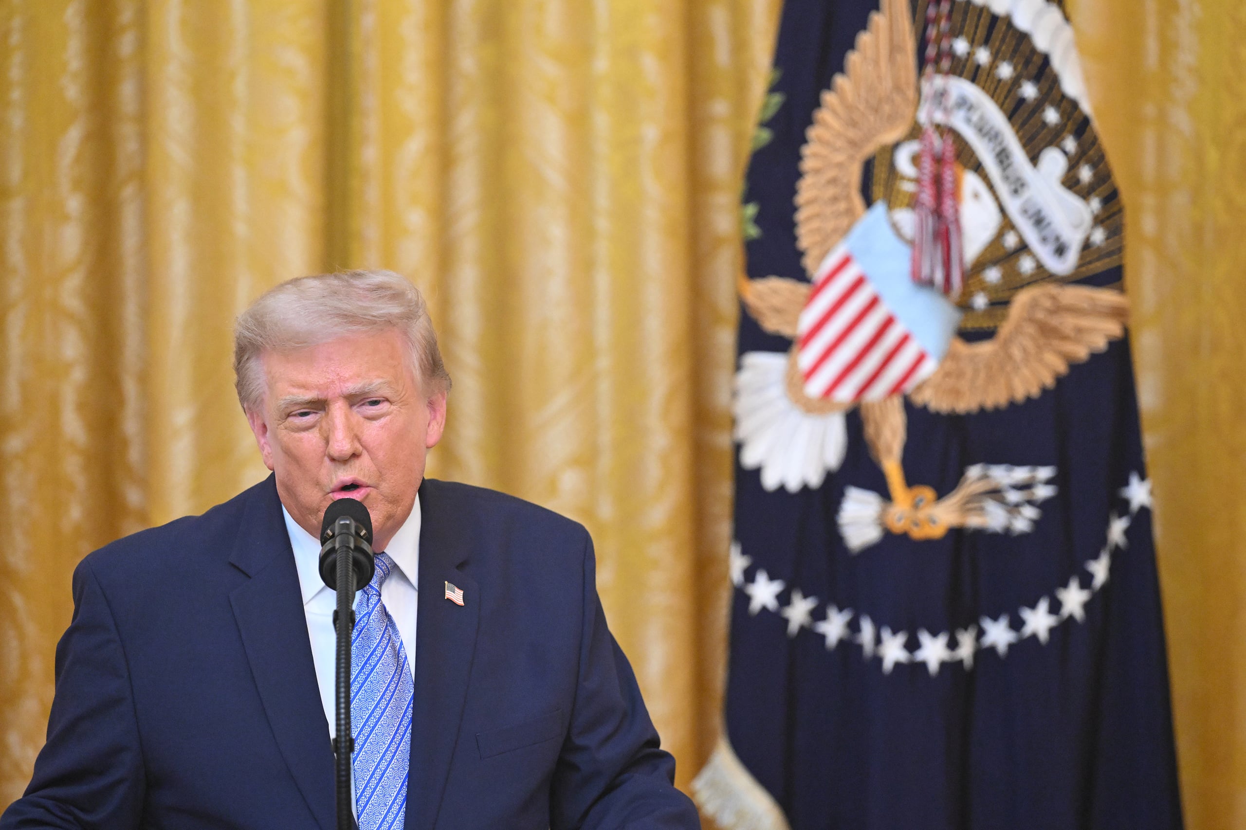 President Donald Trump gives a speech next to a flag and against a yellow cloth background.