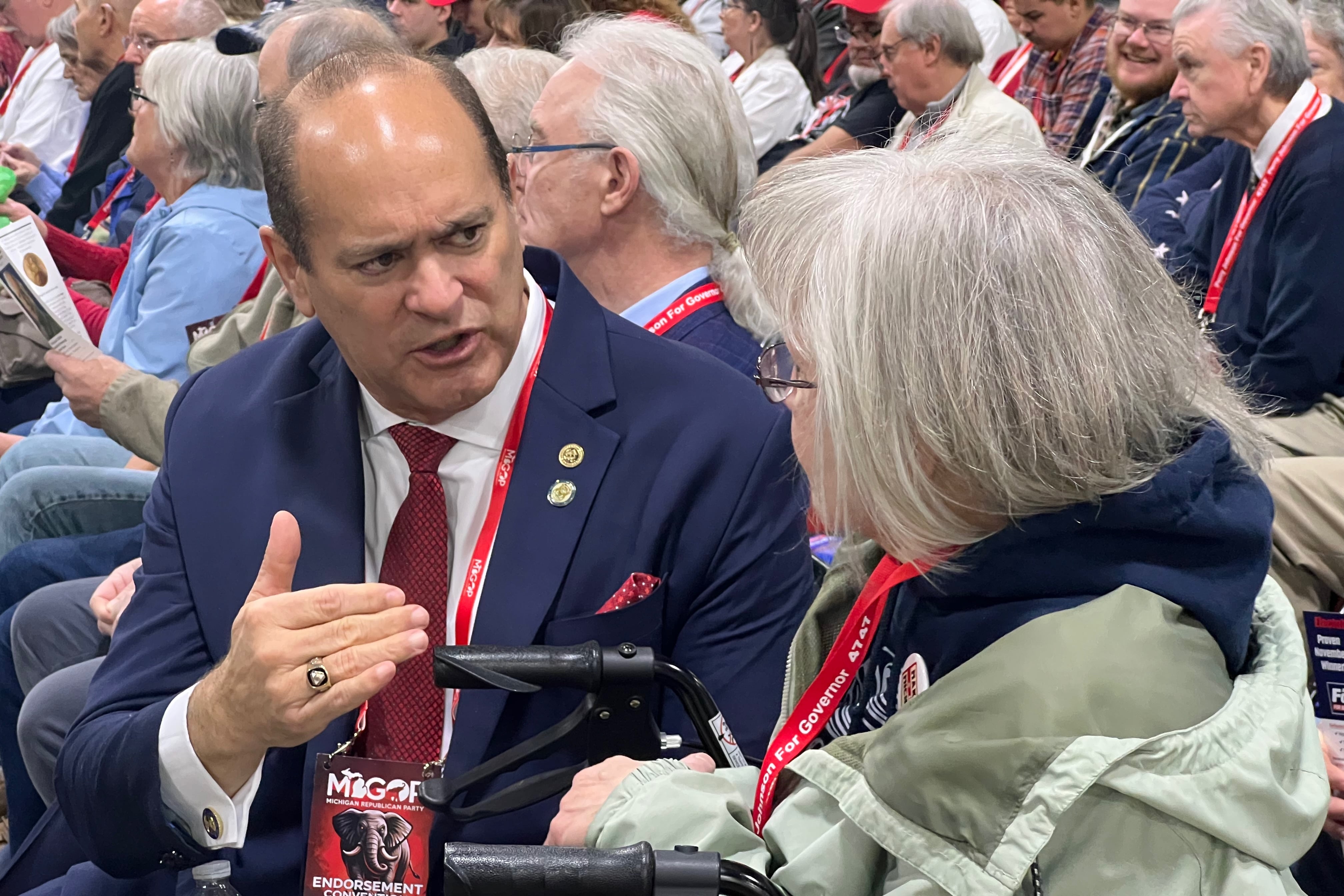 A man in a suit and tie talking and gesticulating next to a woman in a jacket.