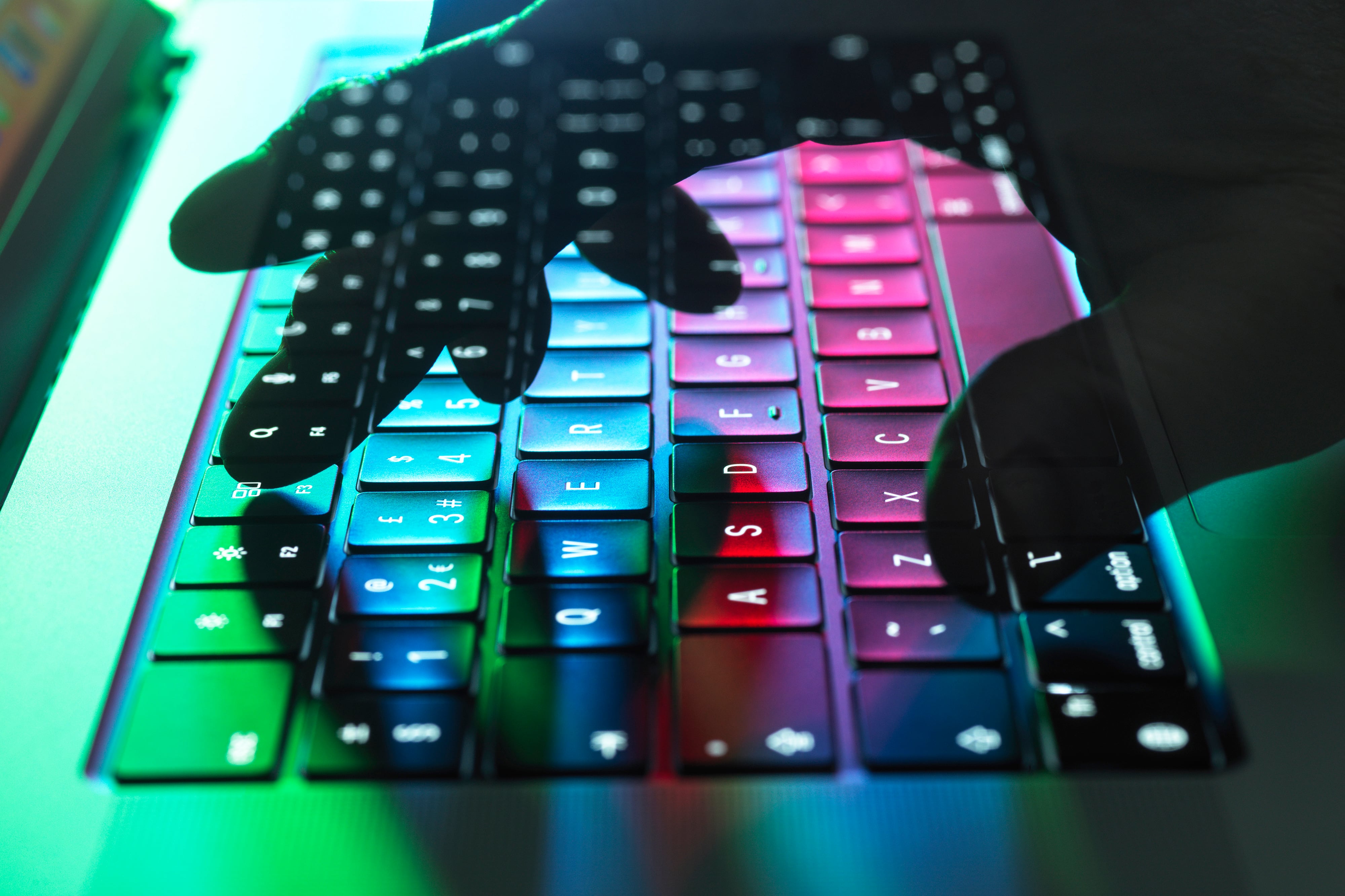 A hand typing on a laptop with lights shining on the keyboard.