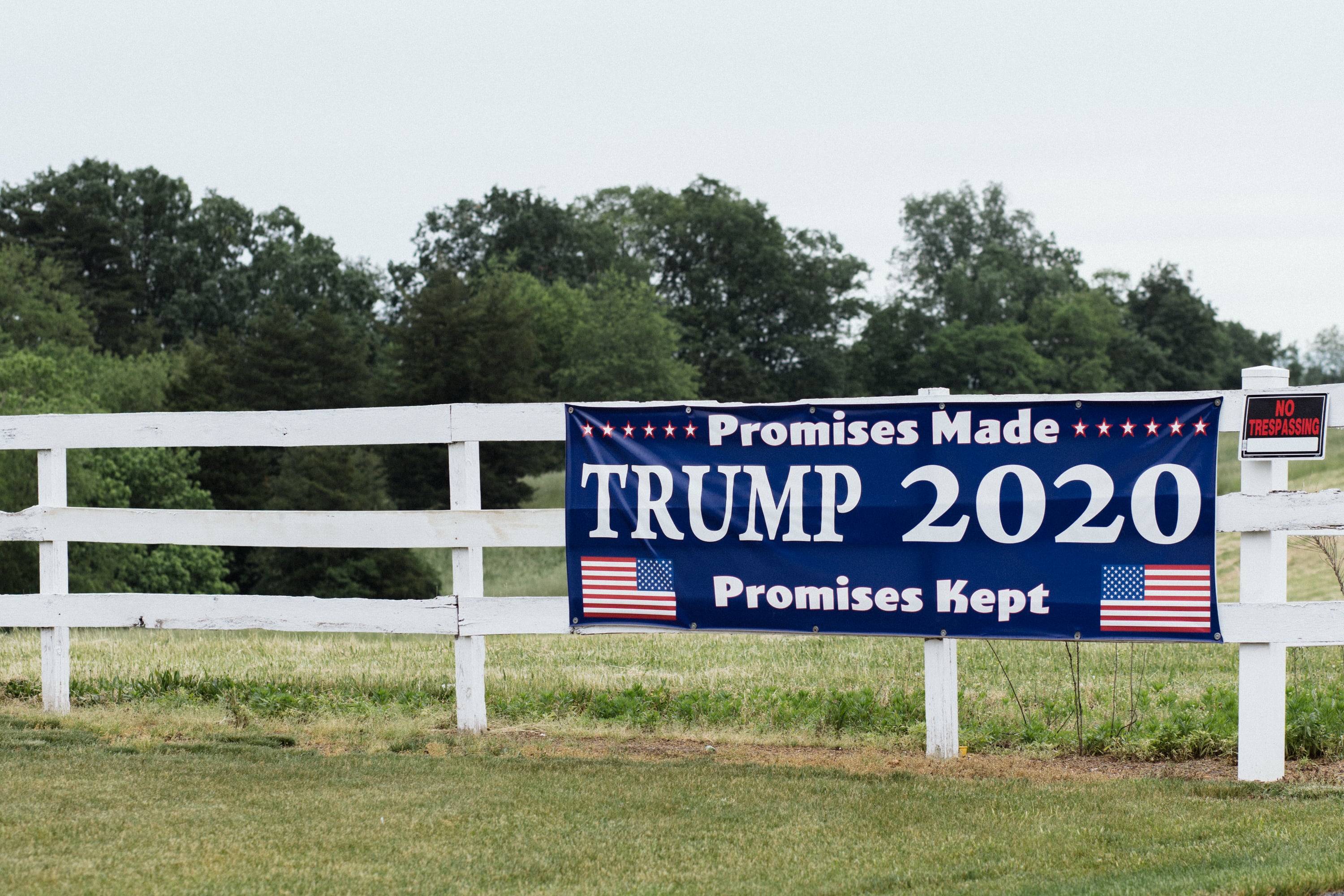 A Trump campaign sign on a white fence.