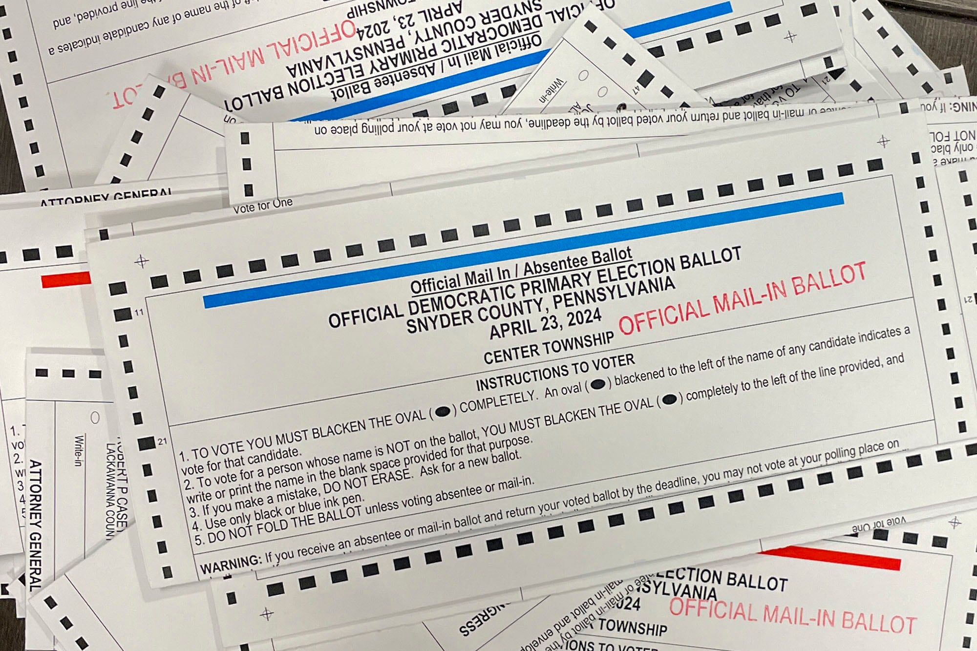 A stack of ballots spread out with white, blue, red and black ink.