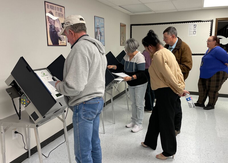 A group of people stand in a small room near voting booths.
