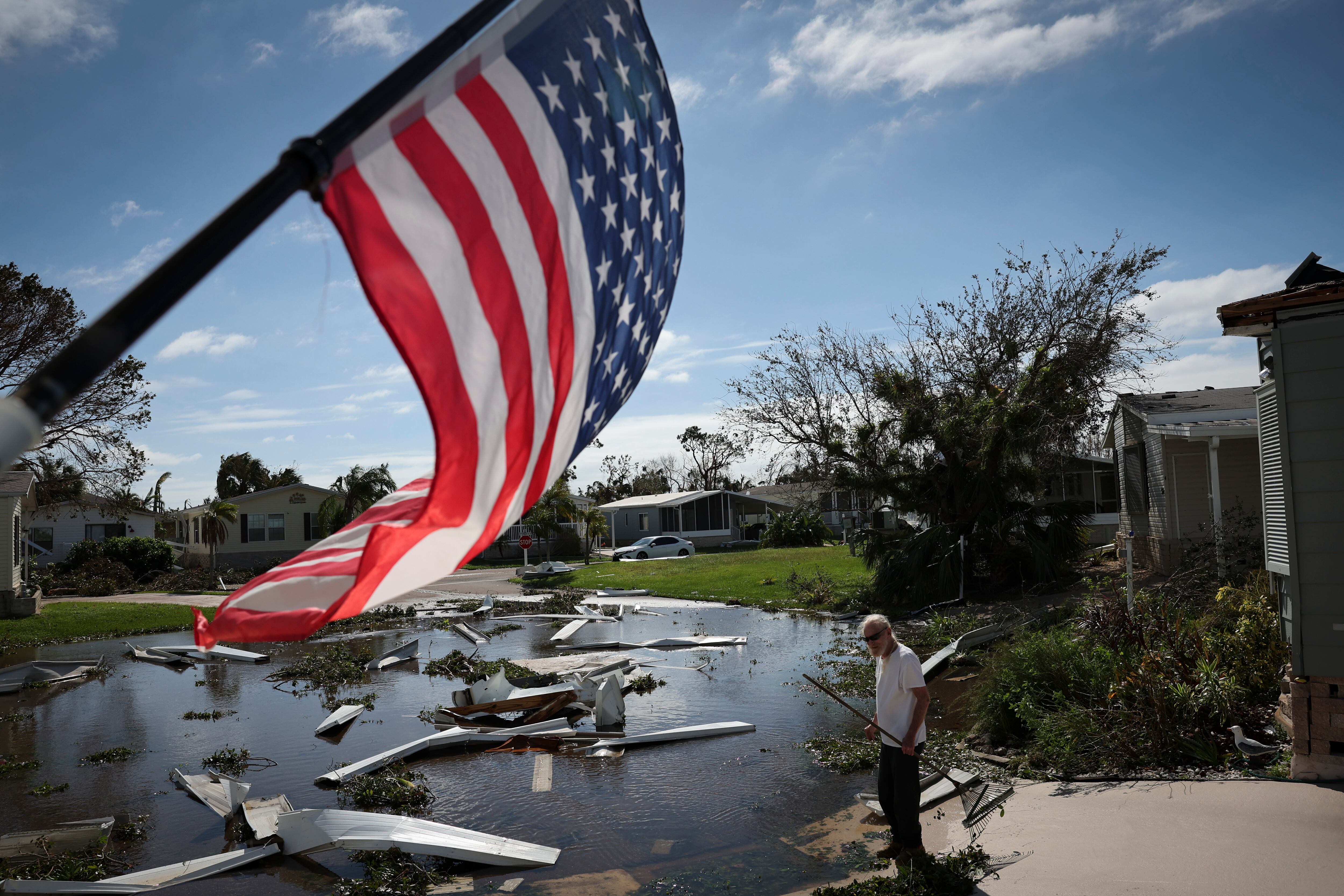 A man gazes at wreckage floating in a pond in front of him, with an American flag in the foreground.