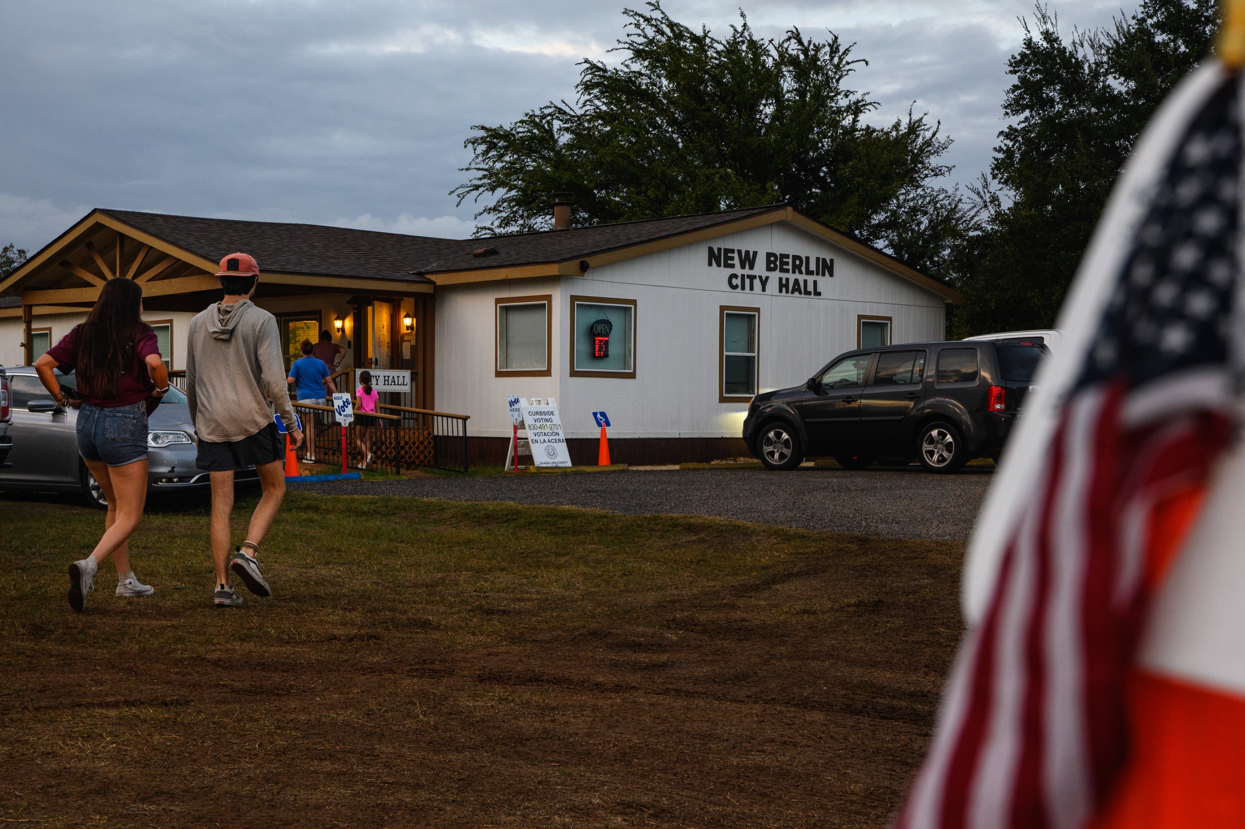 People make their way from a parking lot in a field to a small building marked as a vote center