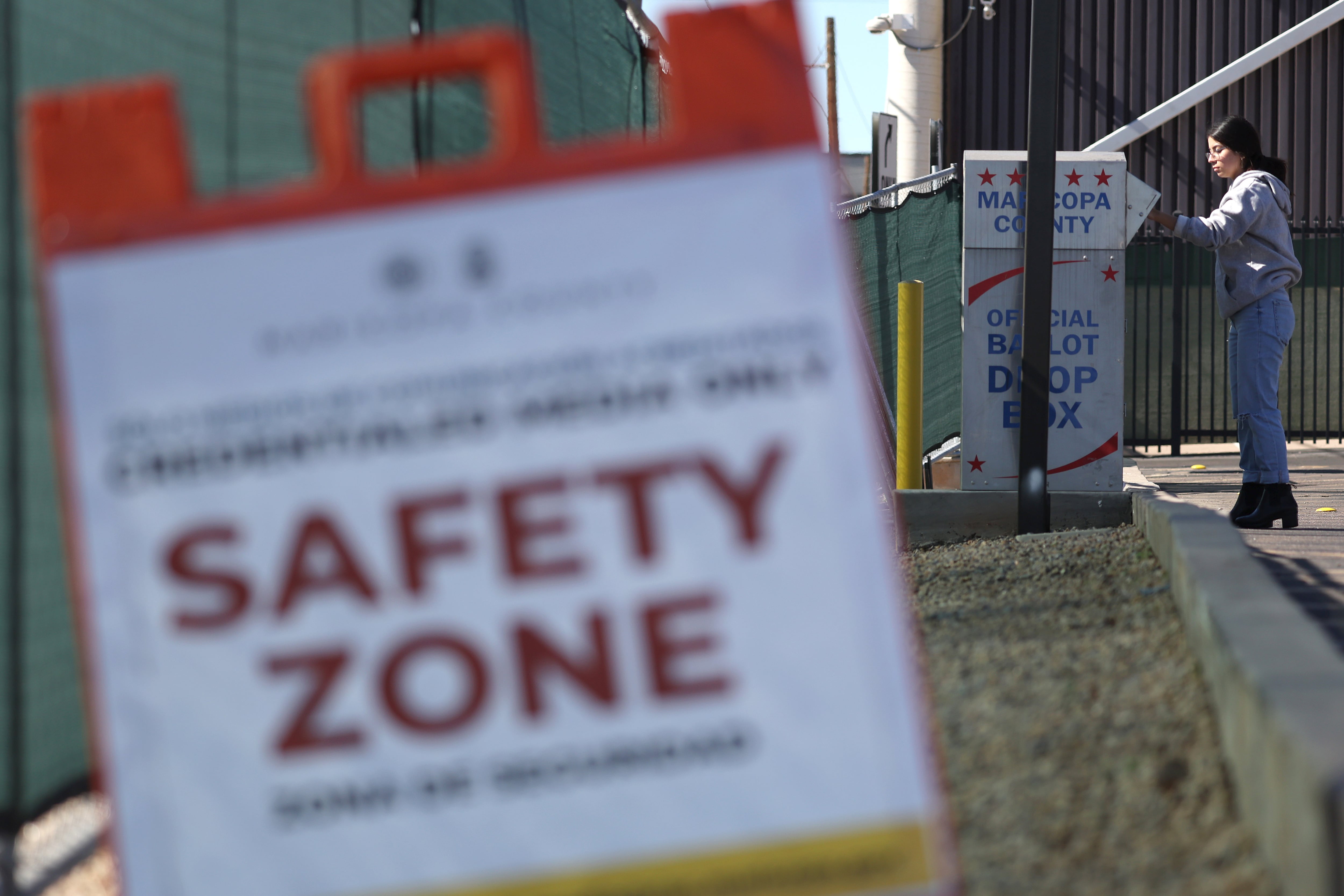 A person drops off their ballot outside a ballot drop box in the background with a sign in the foreground.