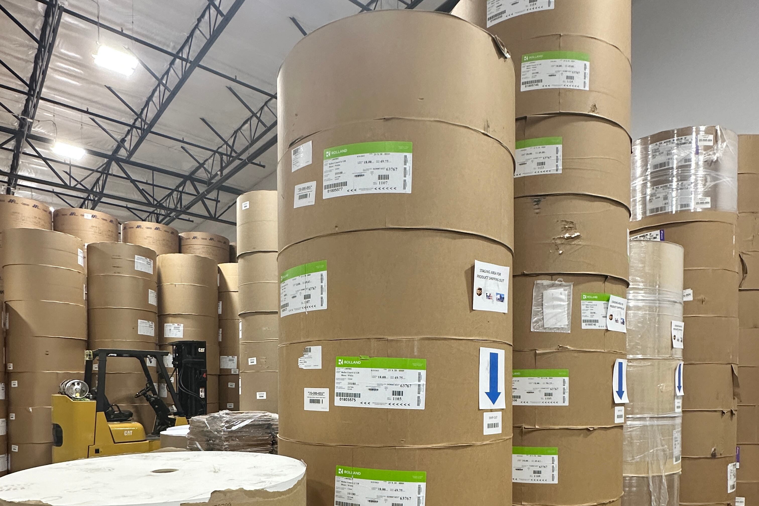 Stacks of giant brown rolls of paper in a warehouse.