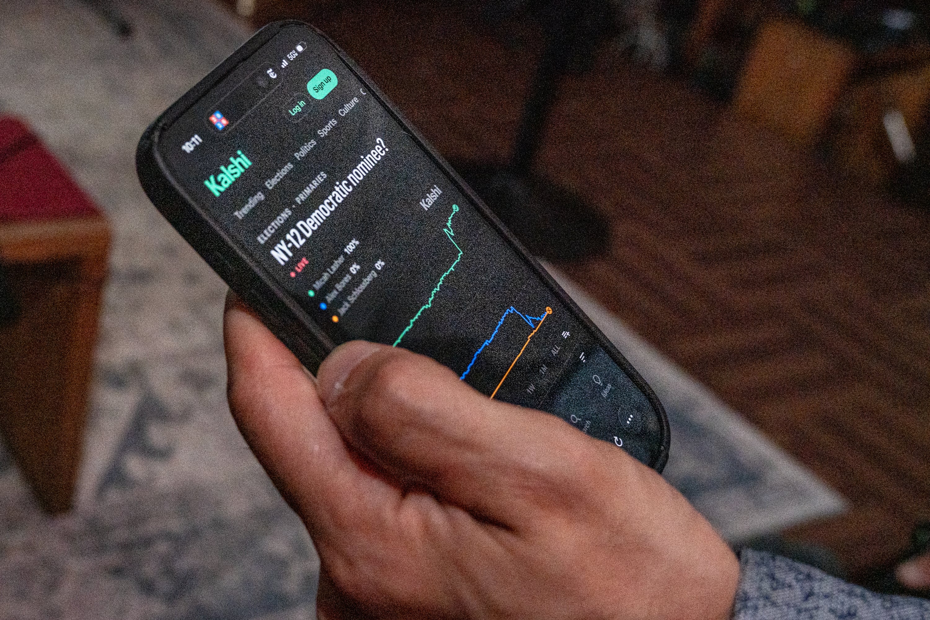 A hand holds a phone with prediction market Kalshi on the screen.