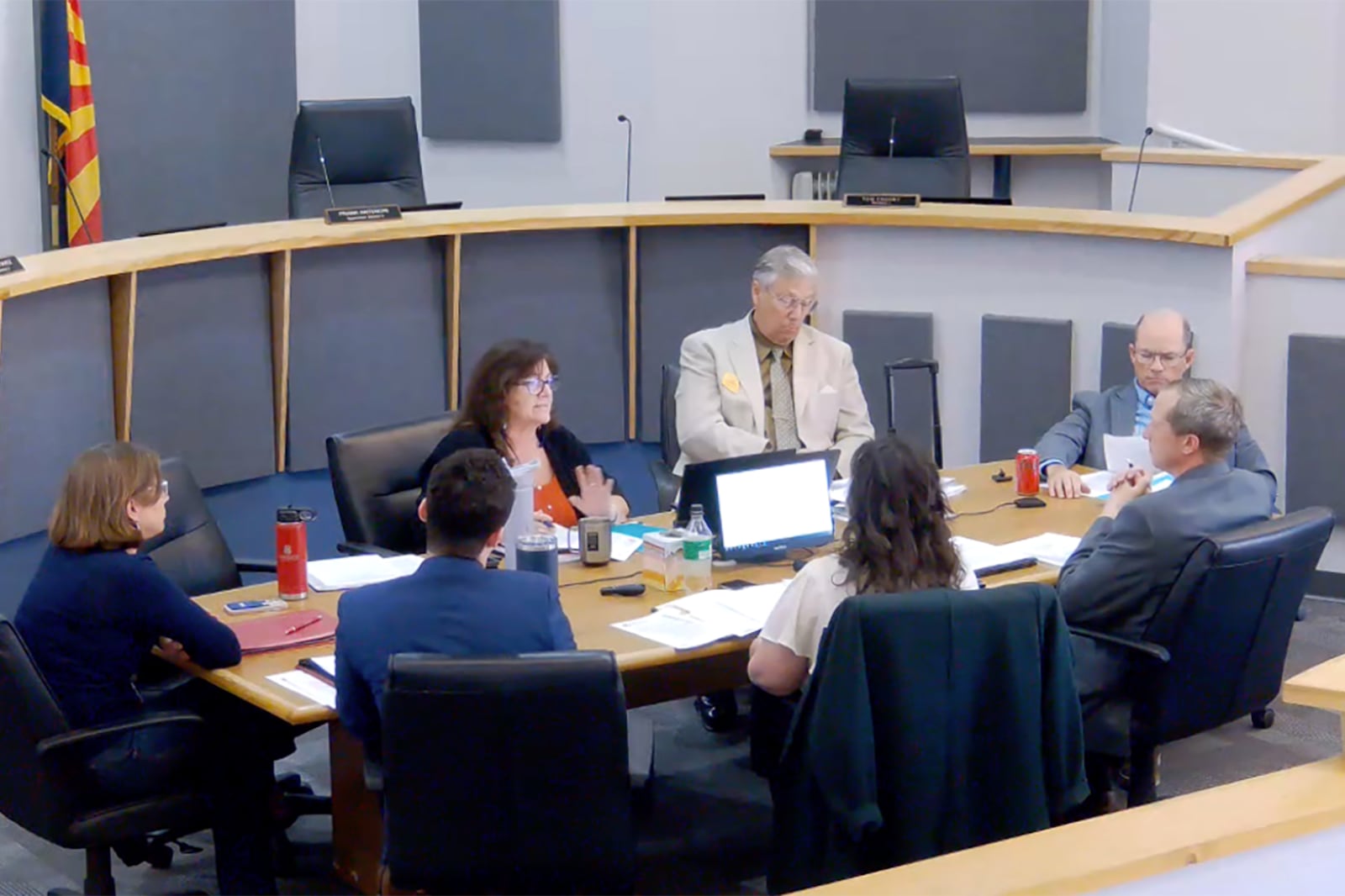A screen grab a group of adults sitting around a round table in a conference room.