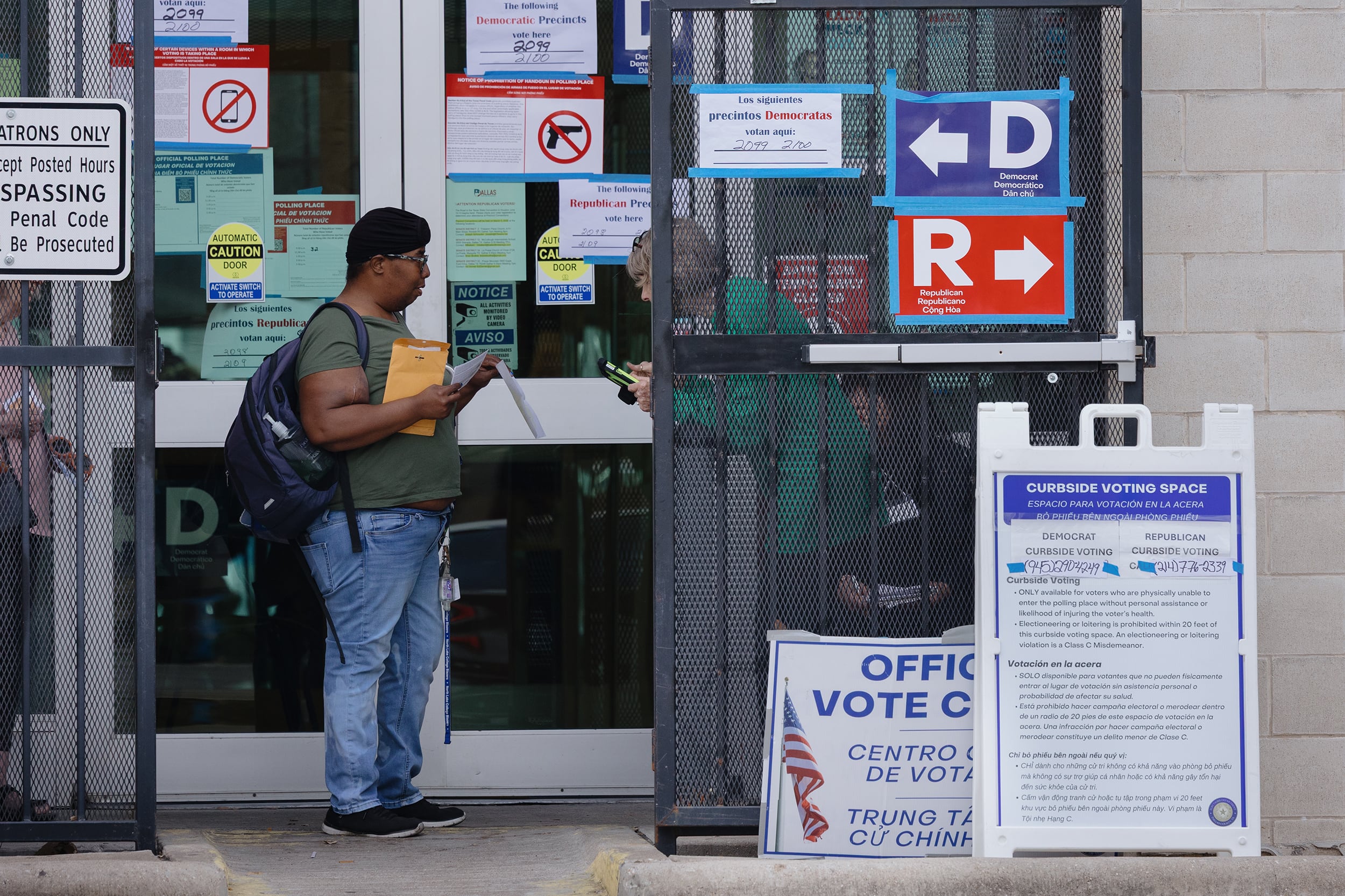 A photograph of two people talking with each other outside of a building that has a ton of posters and signs.