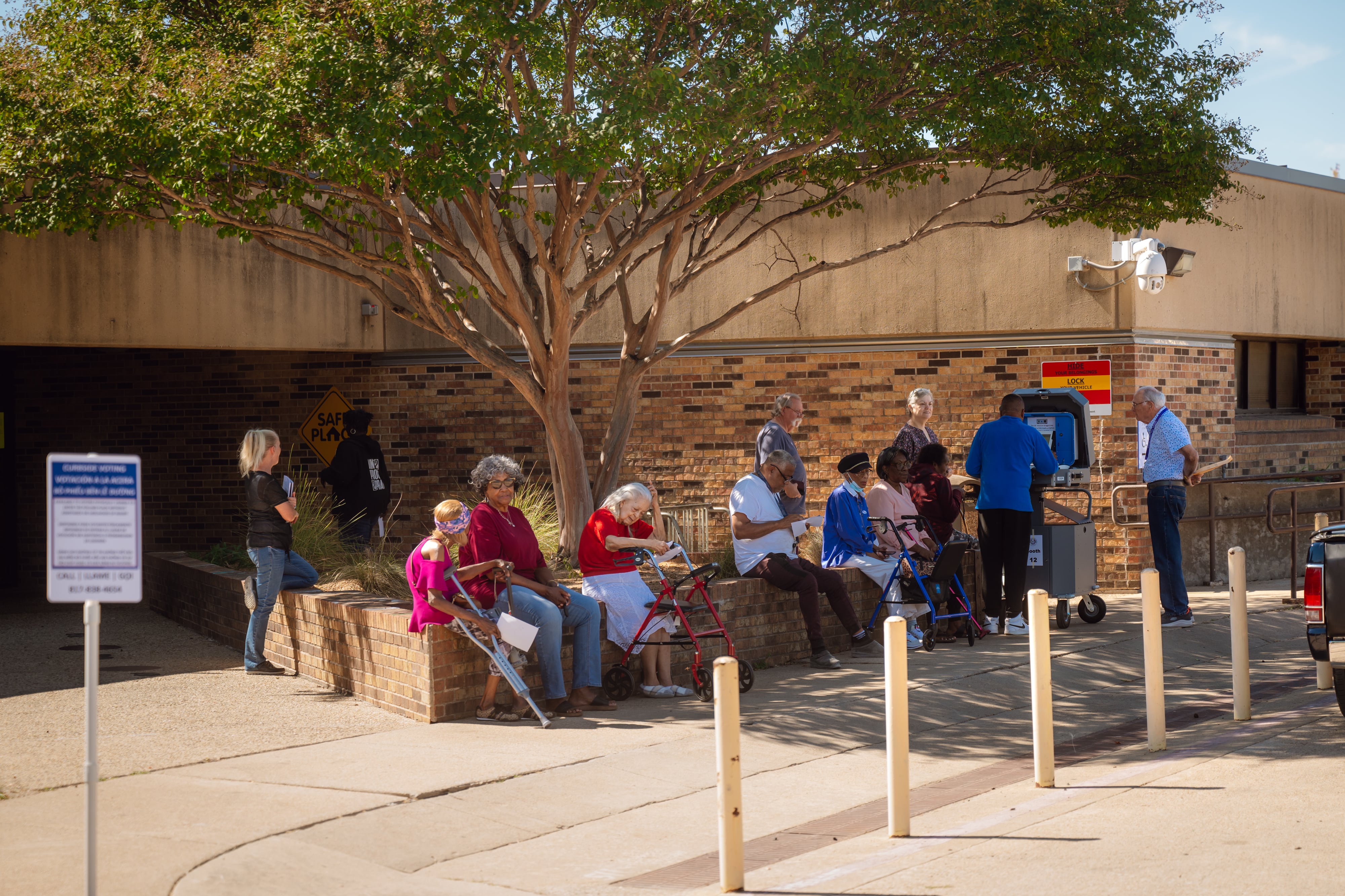 A group of people sit outside while a man does curbside voting.