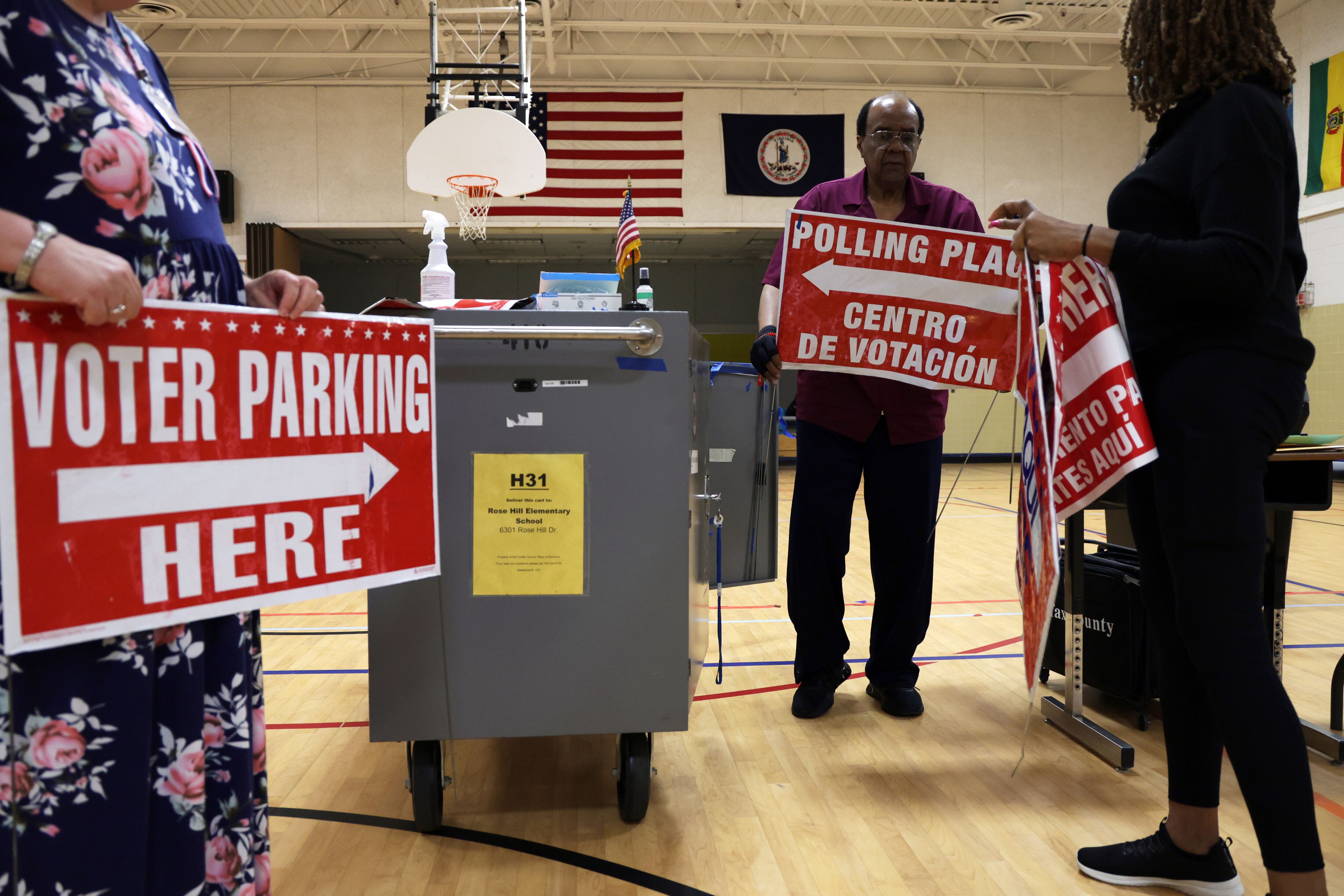 Three people stand in a circle holding red and blue signs in a gym.