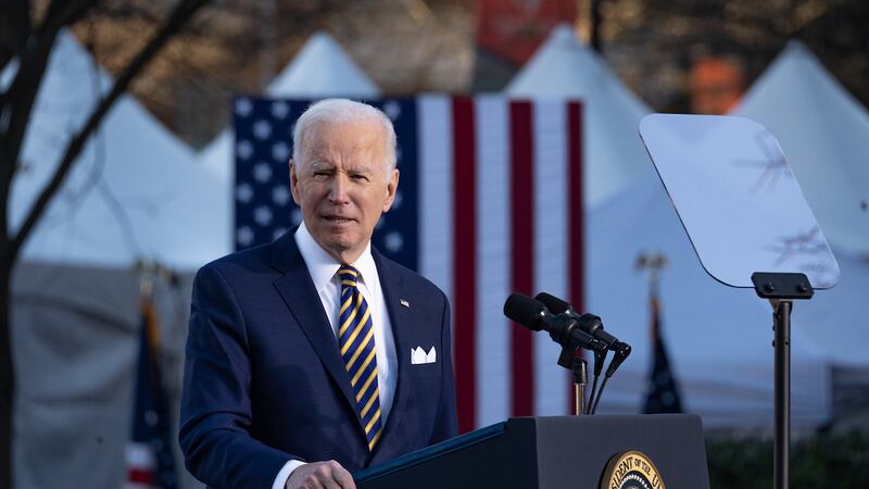 Joe Biden standing outdoors at a lectern, with a U.S. flag behind him