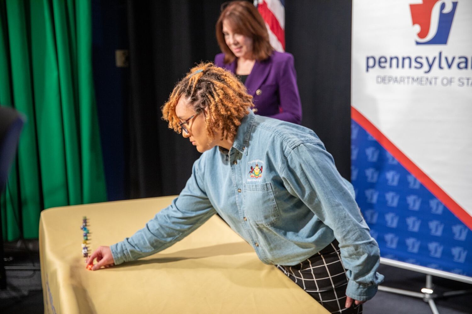 A woman leans over a table to place a die at the end of a row of other dice