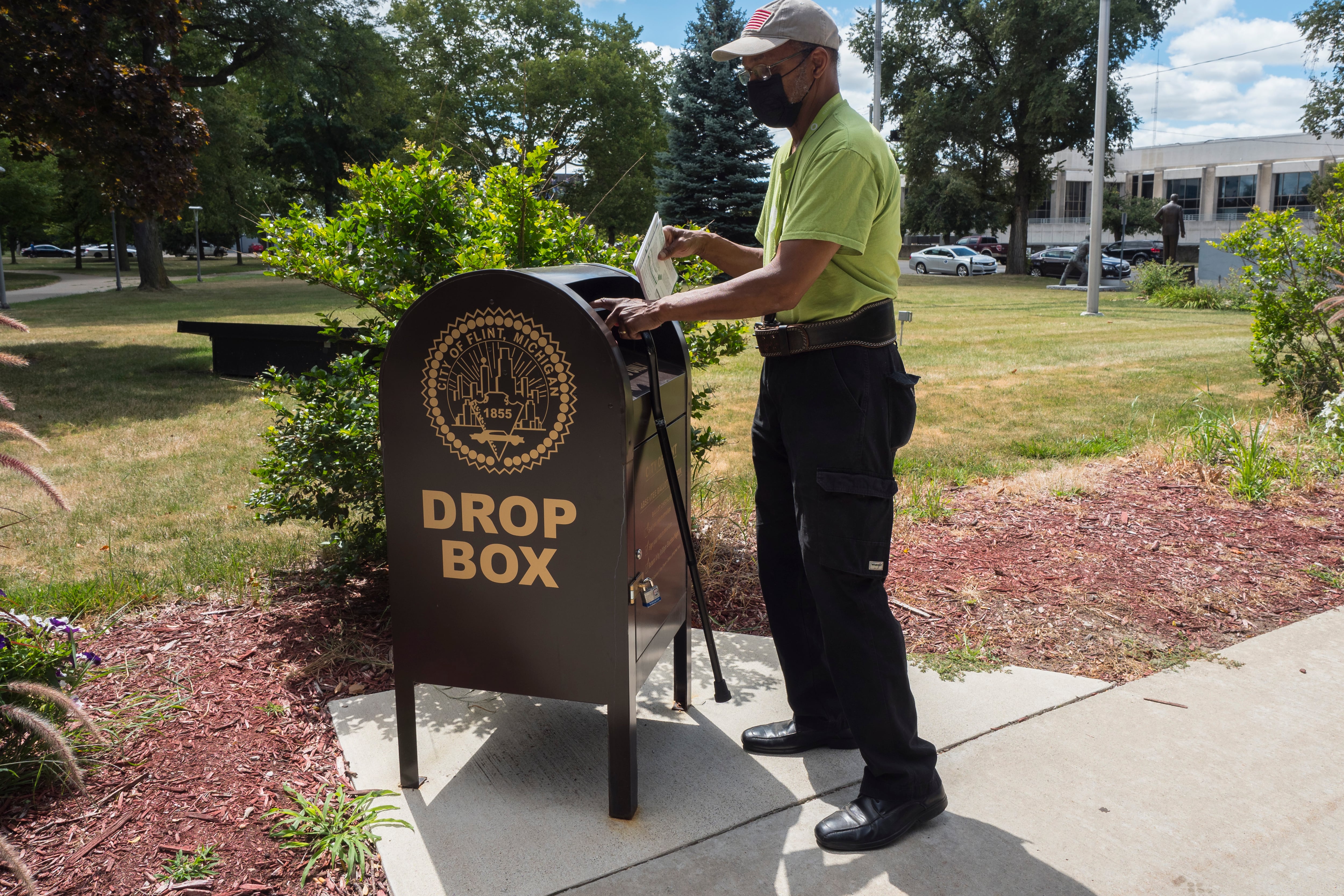 A man inserts an envelope into large brown metal bin on the edge of a public garden.