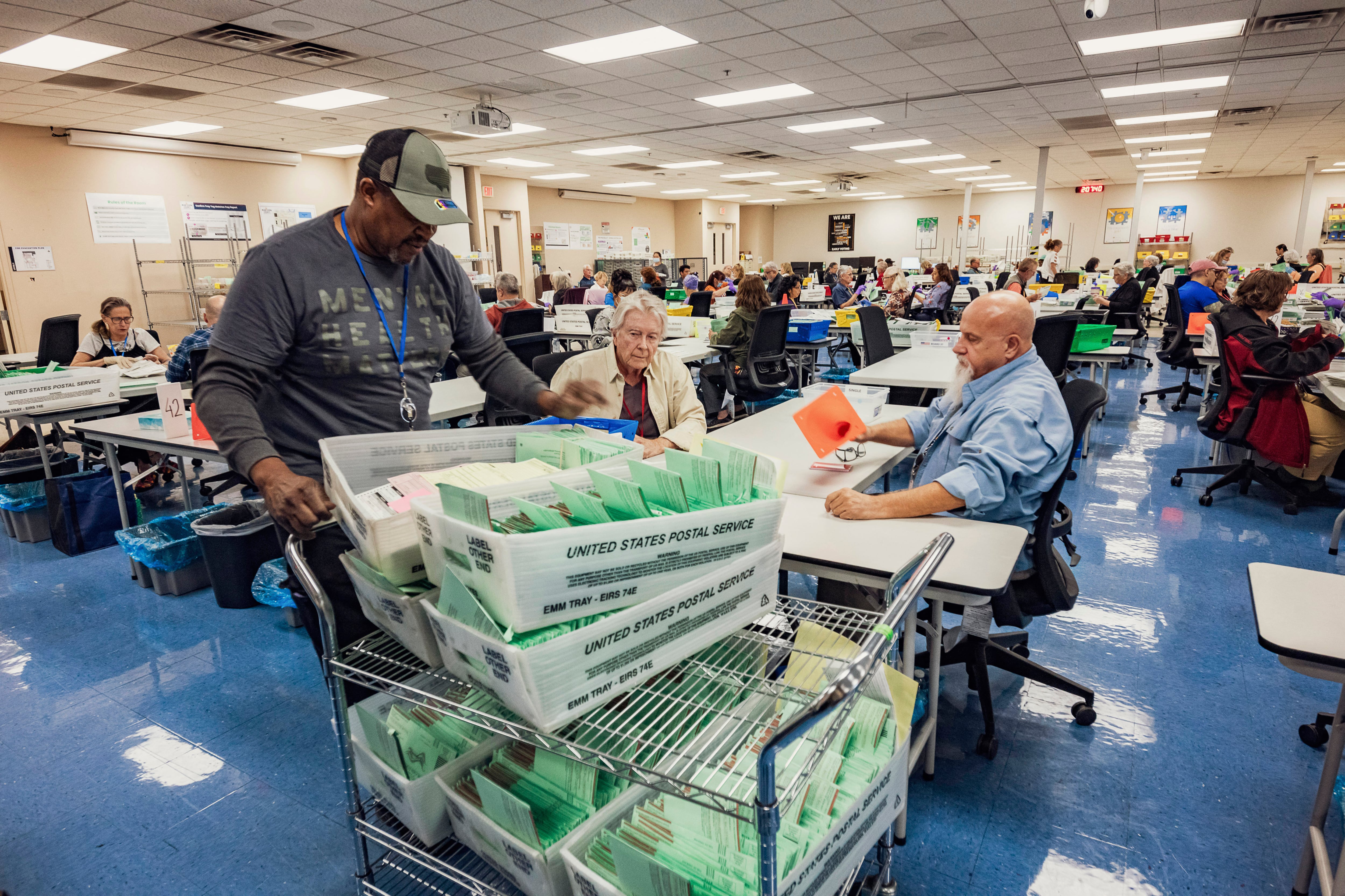 A group of people stand and sit in a large room counting green and white paper.