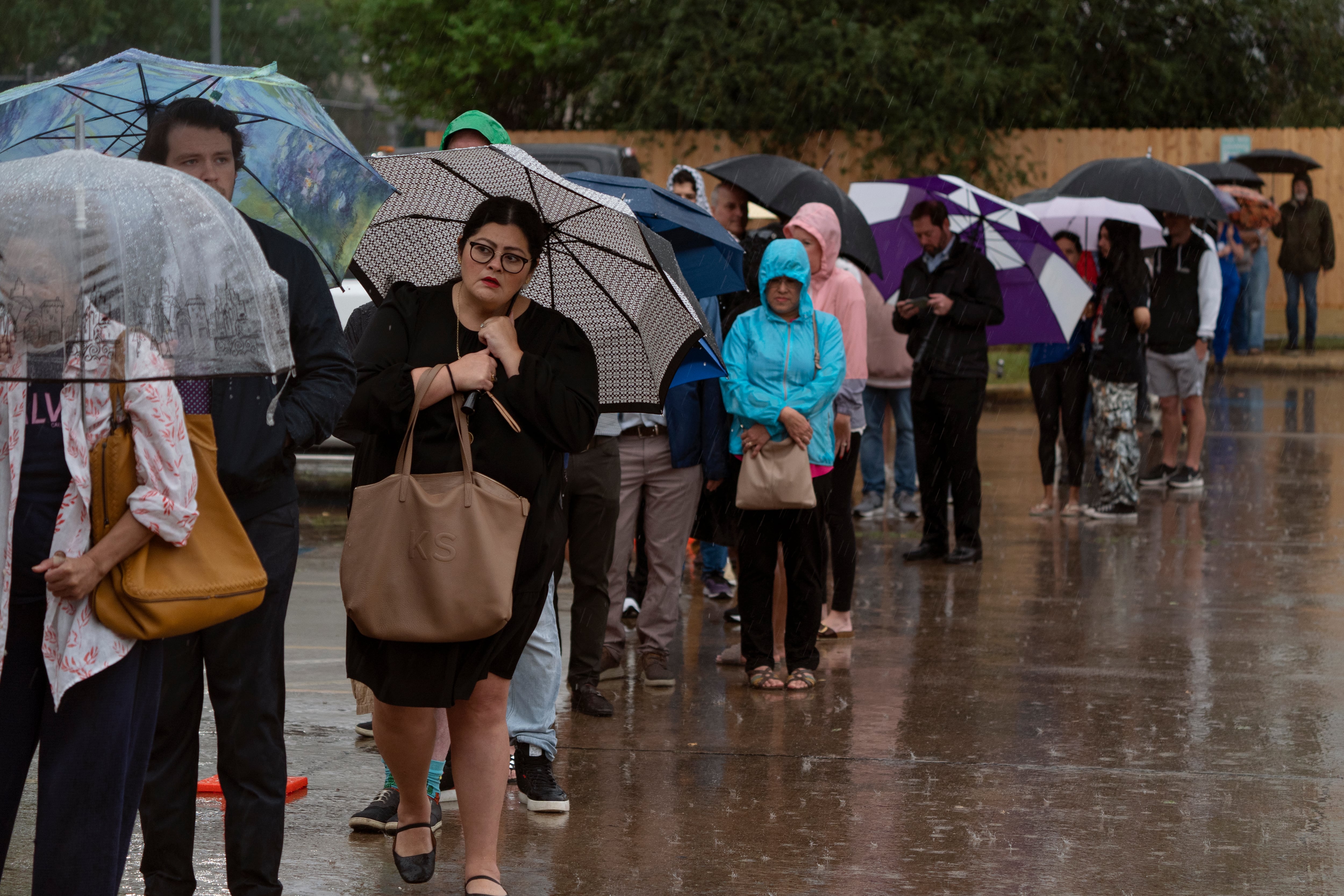 A group of people stand in line; some are holding umbrellas.