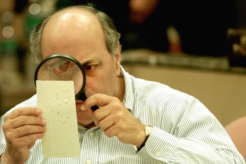 A man holds a magnifying glass to a punch card ballot.