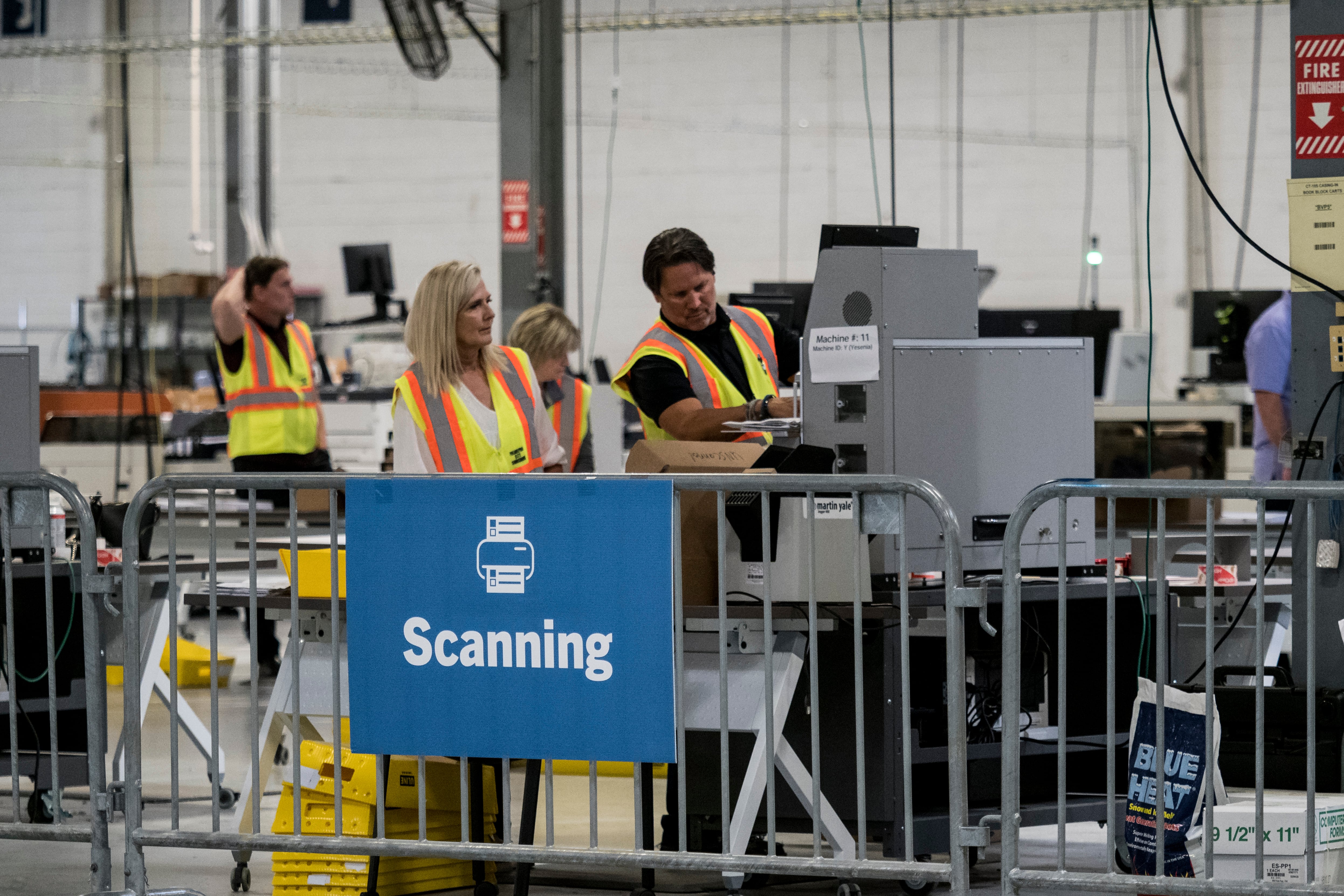Two workers in yellow vest operate a large machine in a warehouse space