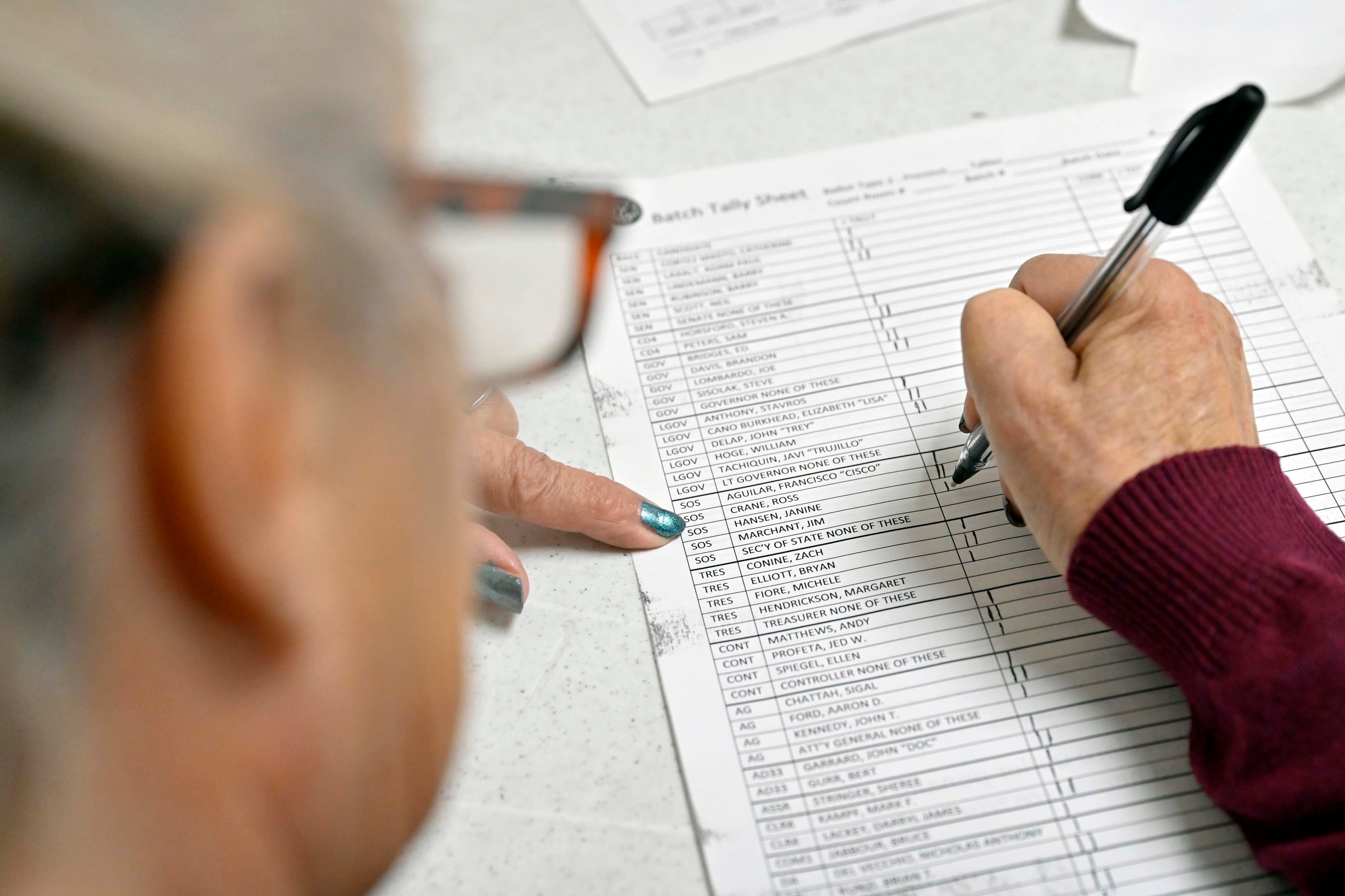 A closeup of a woman’s hand as she uses a pen to mark a lined, paper form