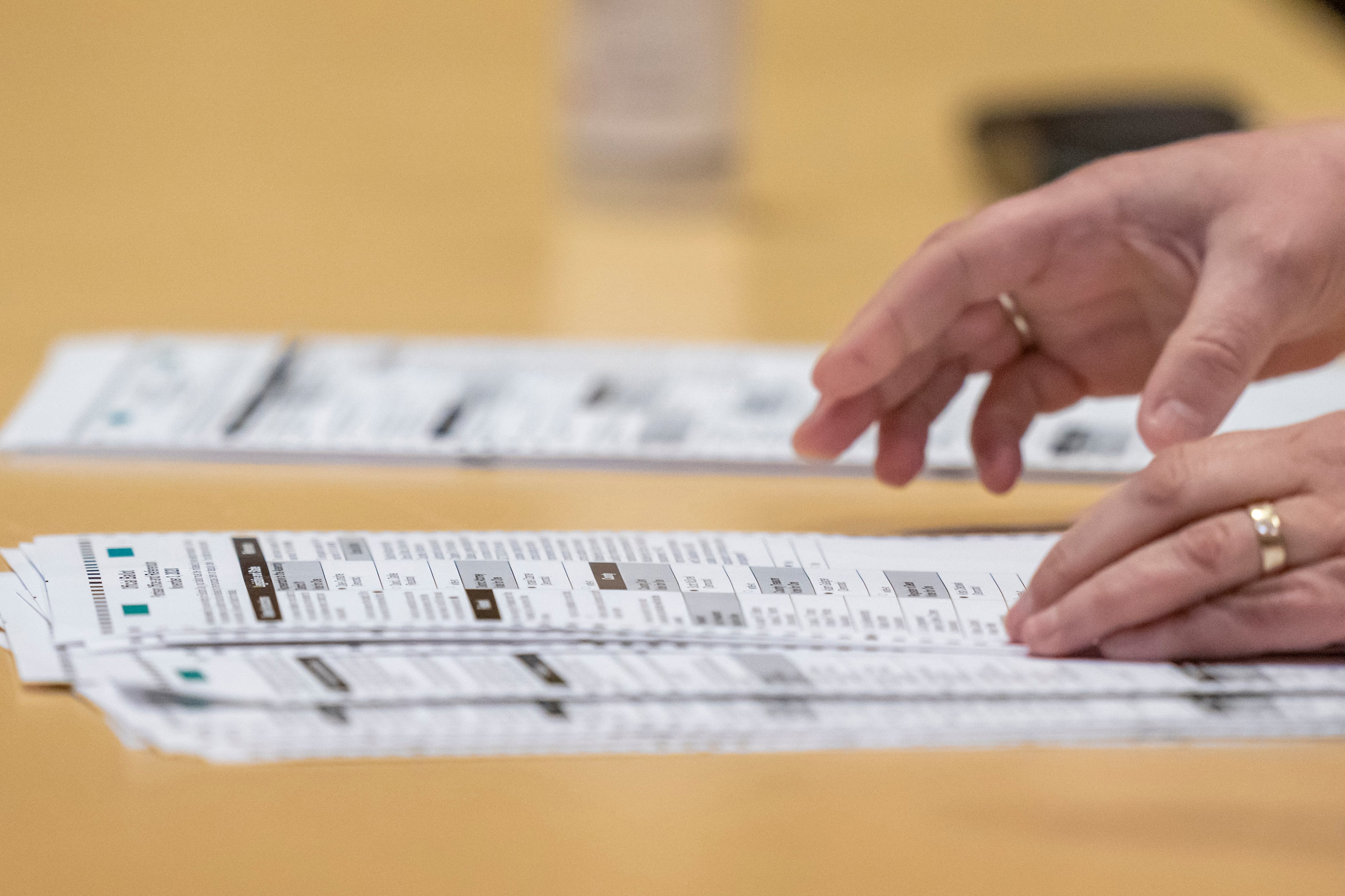 A close up of a pair of hands over a stack of ballots on a wooden table.