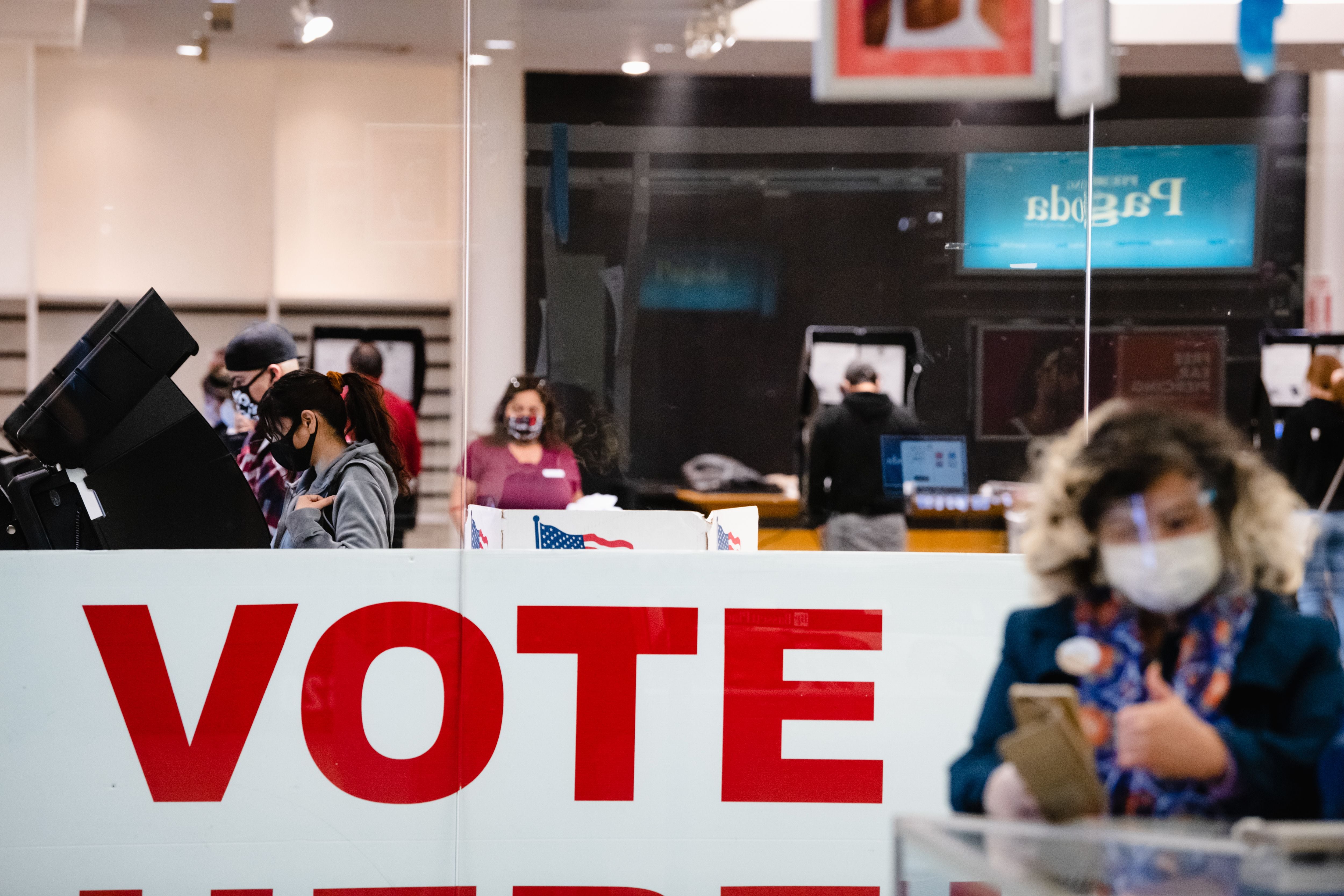 A large “vote” sign with people inside a room with voting booths