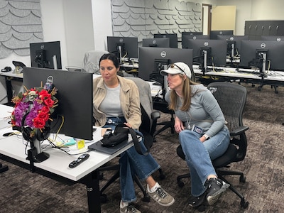 Two women work from behind a computer in a large room.