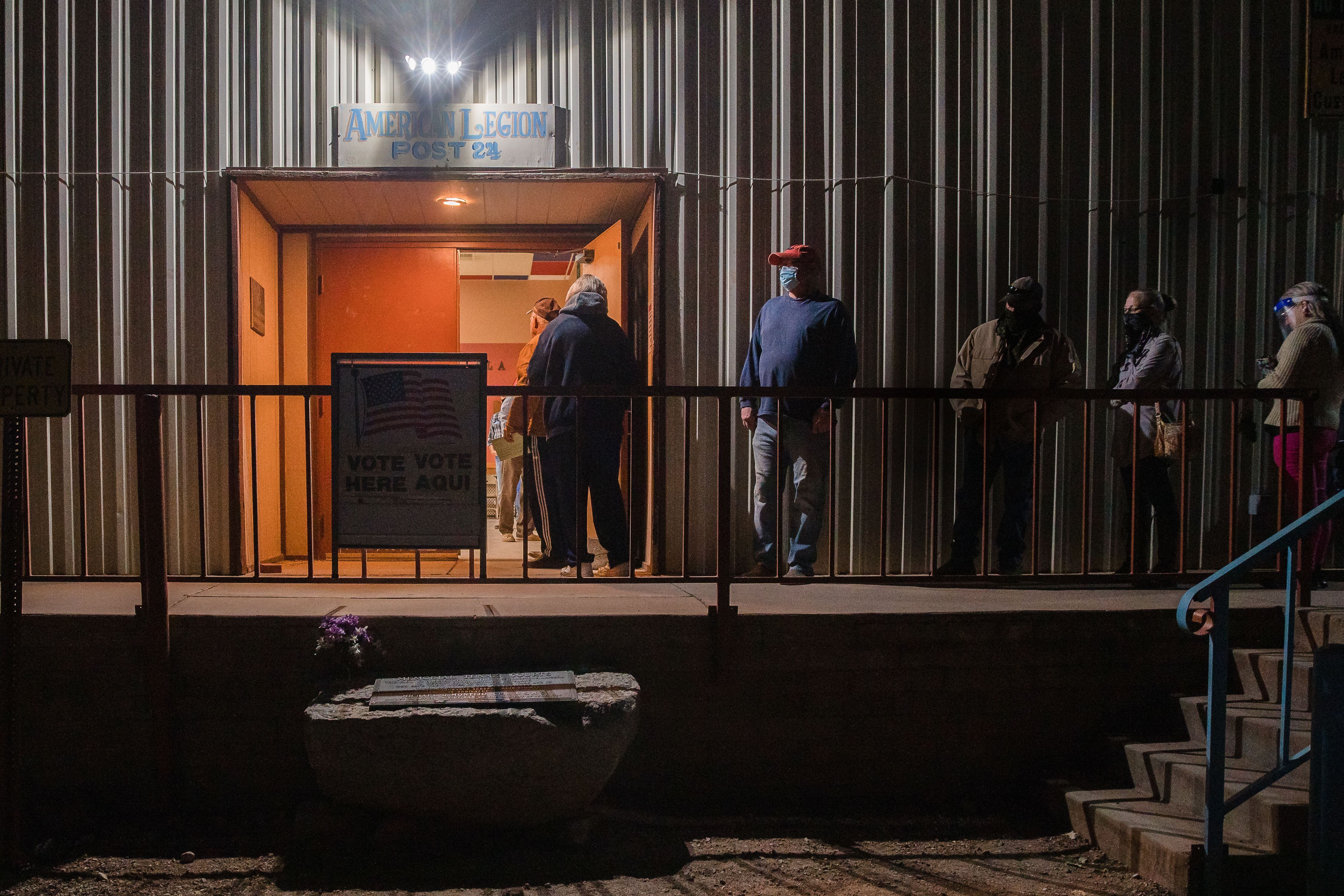People wait in line outside a building in the dark.
