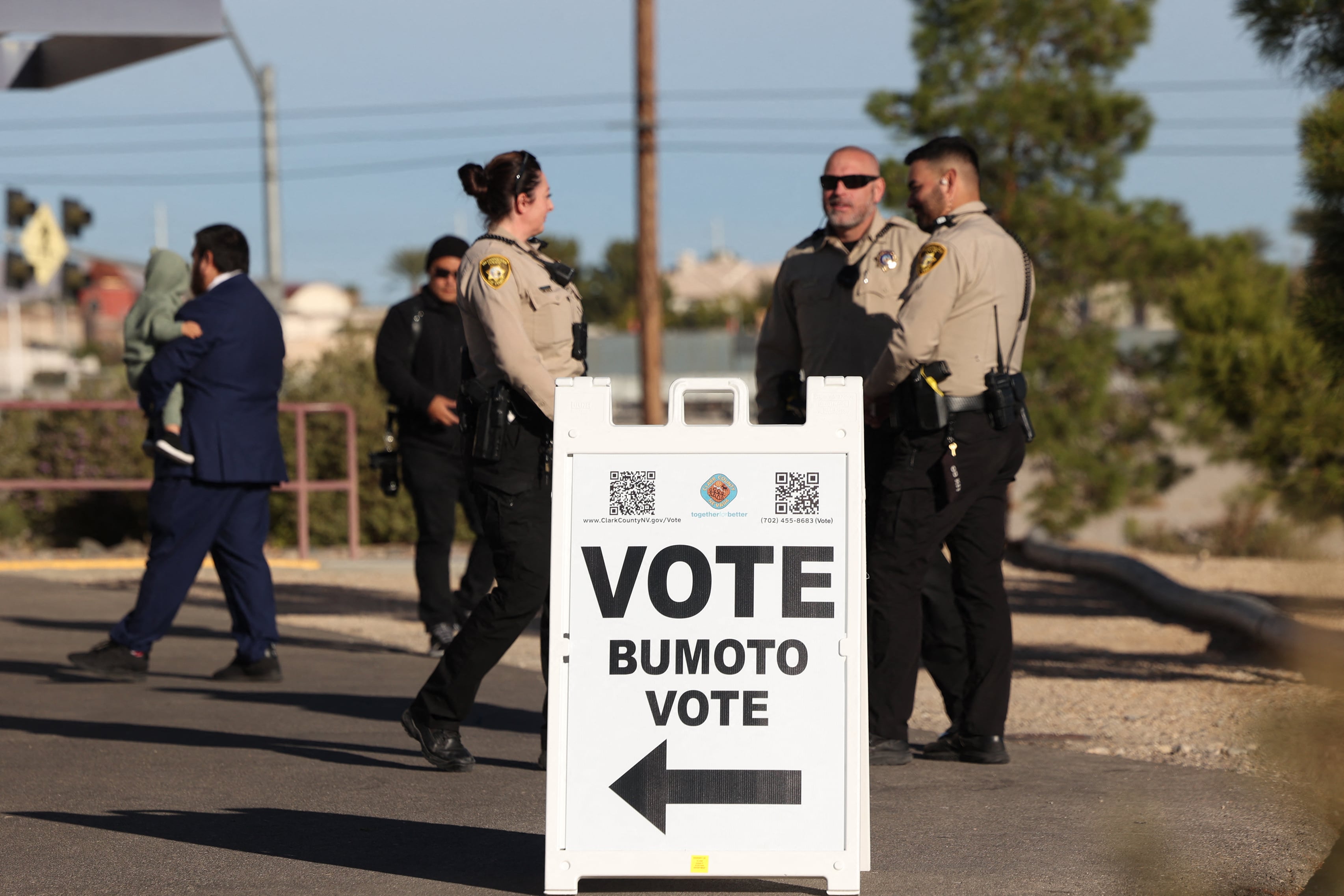 Law enforcement personnel stand behind a vote sign.