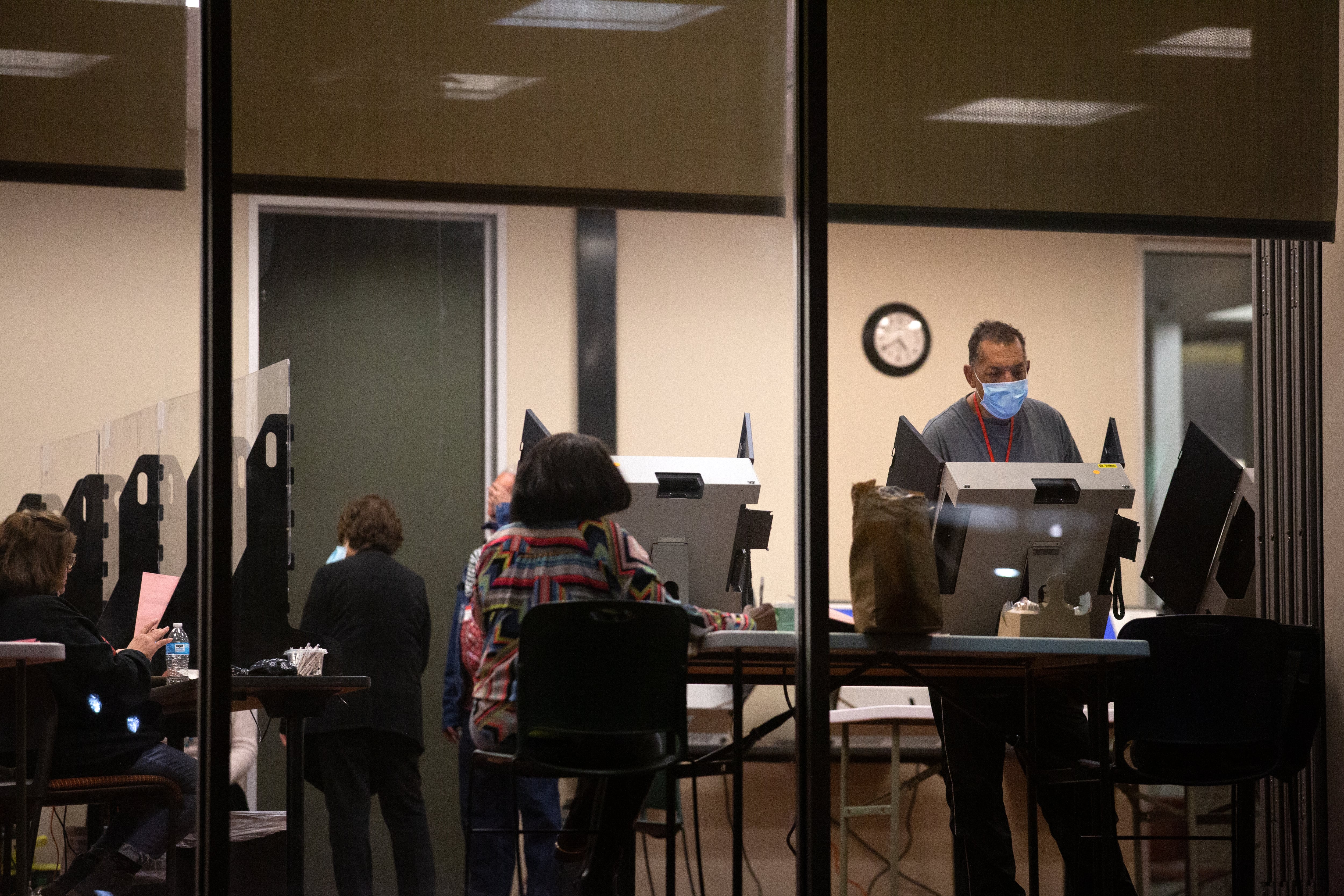 A man inside a building stands in front of a row of voting machines