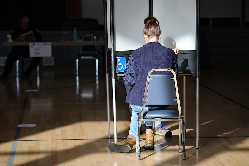 A woman sits at a polling booth in side of a room.