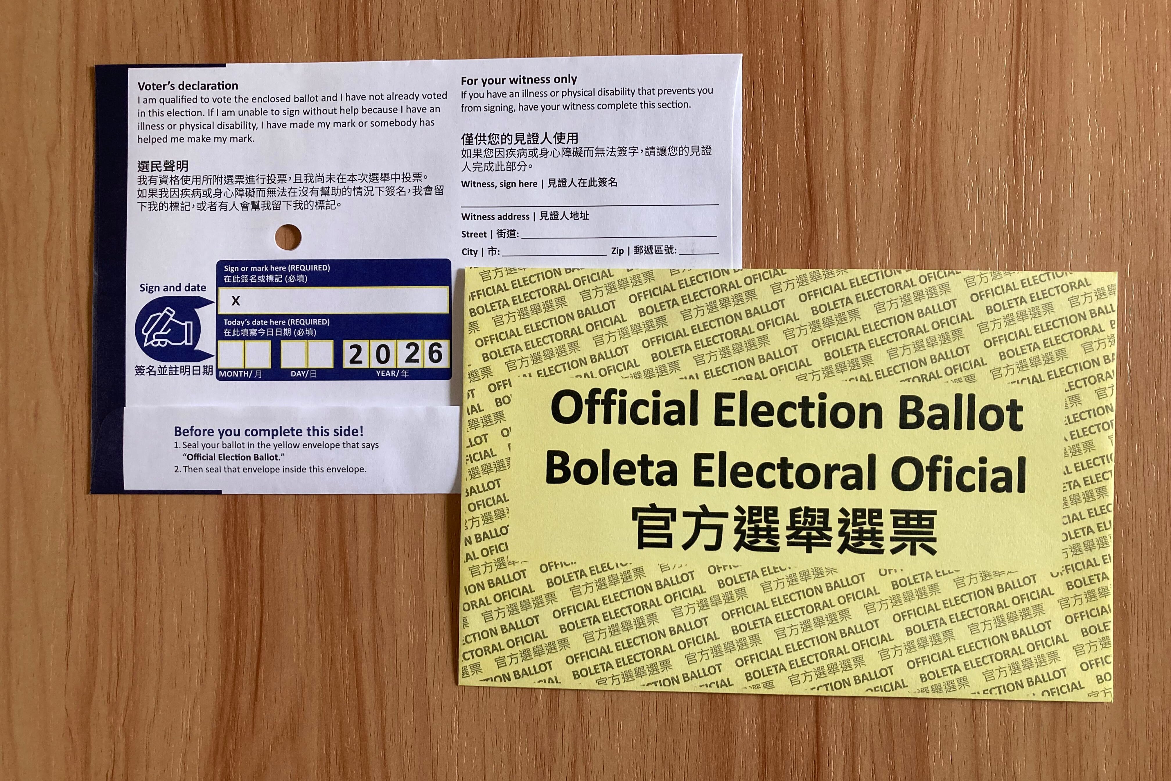 A white mail ballot and a yellow envelope sit on a wooden table.