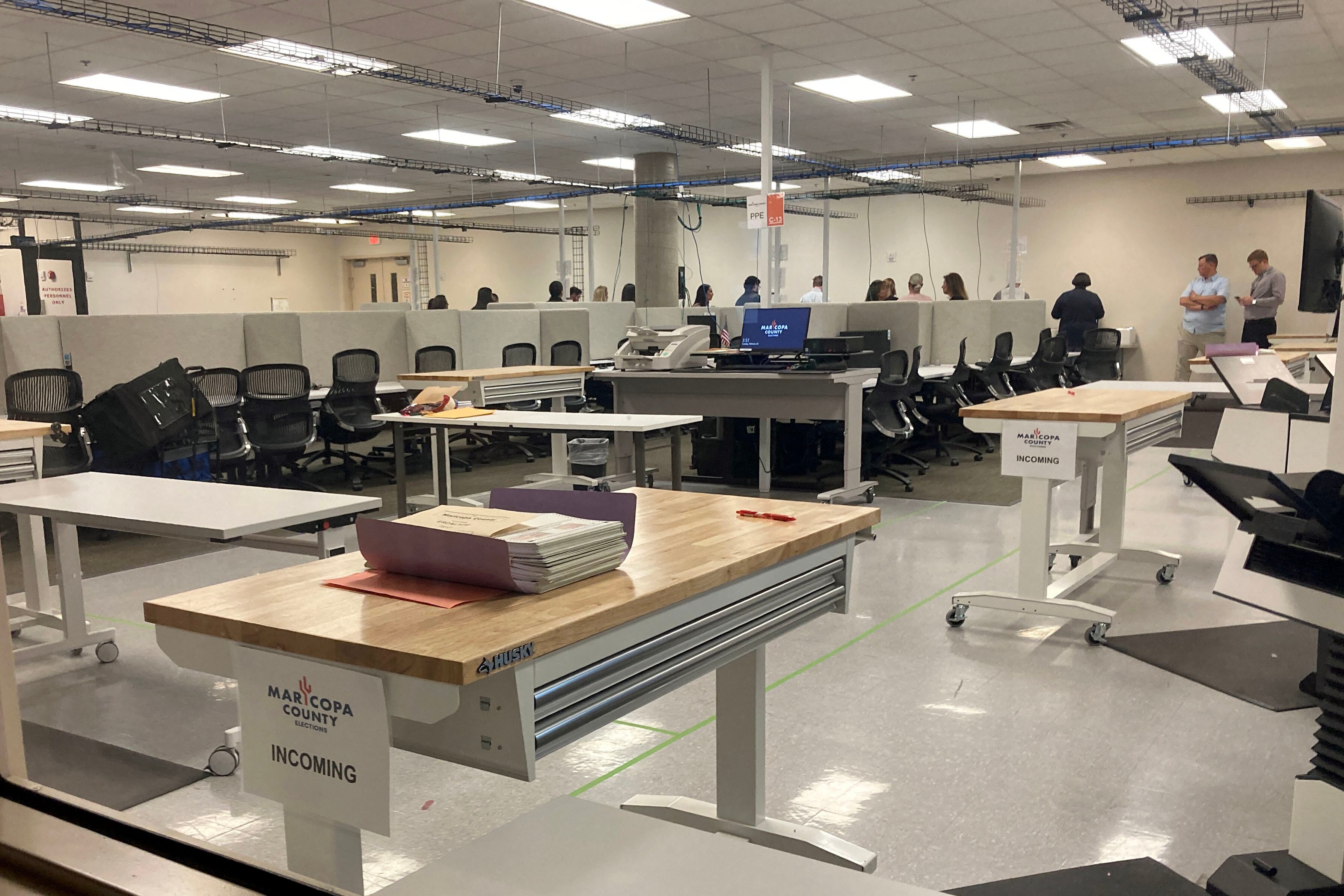 The inside of the Maricopa County election center with tables and machines filling the room with people standing in the background.