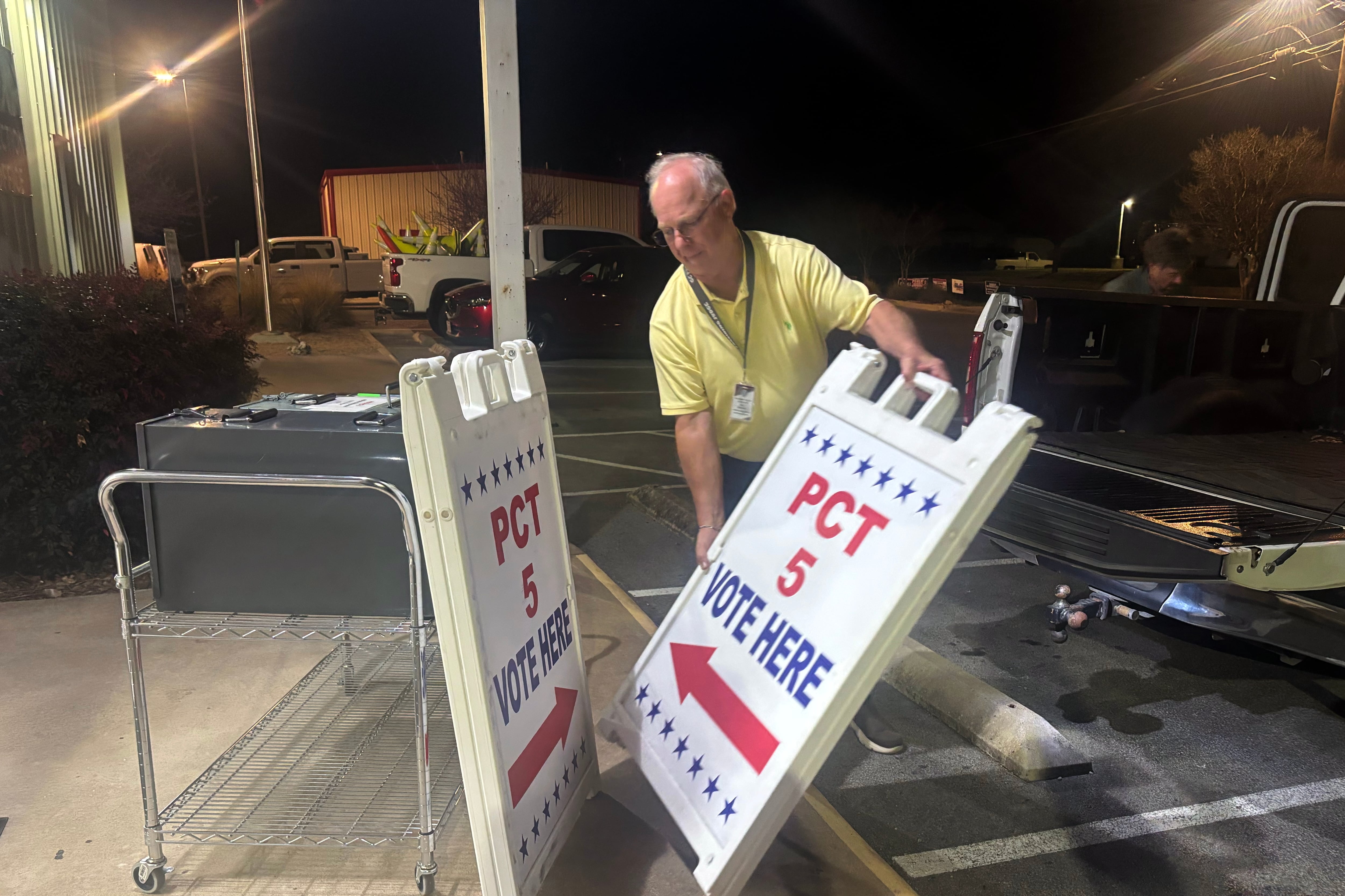 A man wearing a yellow shirt holds a sign leaning against him. The sign is white and reads "PCT 5 VOTE HERE" with a red arrow.