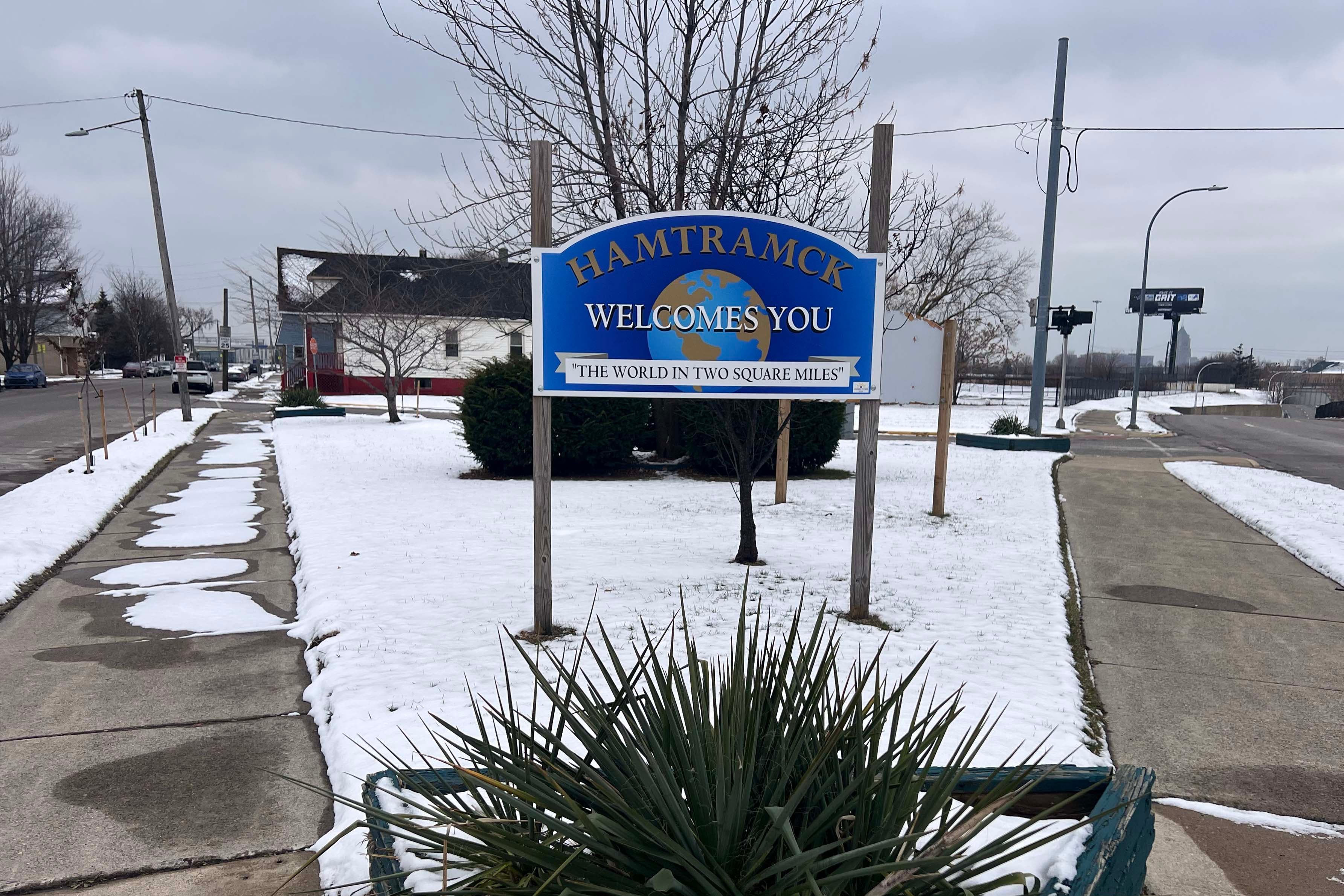 A photograph of a blue and colorful sign that reads "Hamtramck welcomes you" outside on a cloudy day.