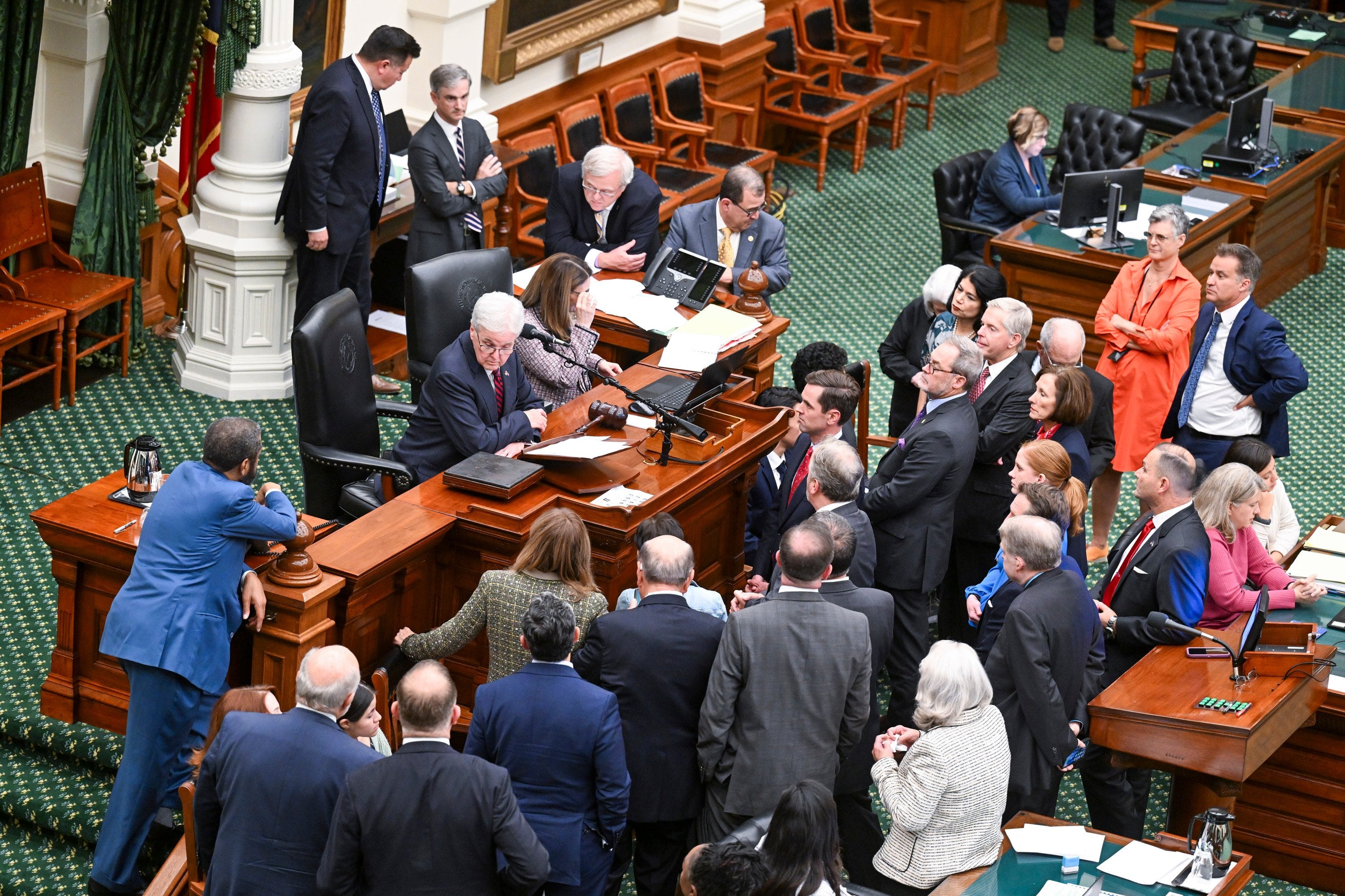 A group of men in suits gather around a desk.