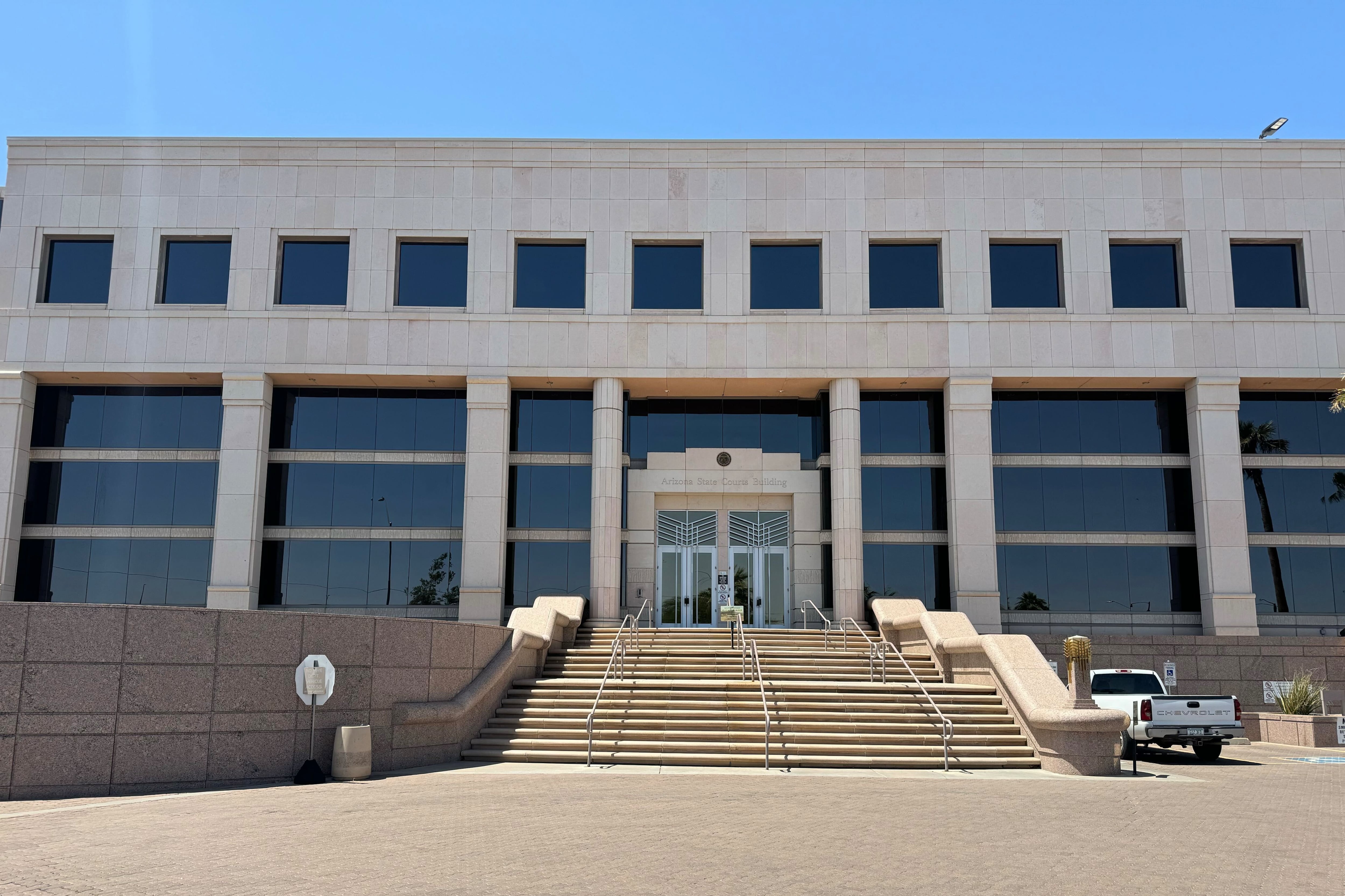 A blue sky and a modern tan building with steps and concrete in front of it.