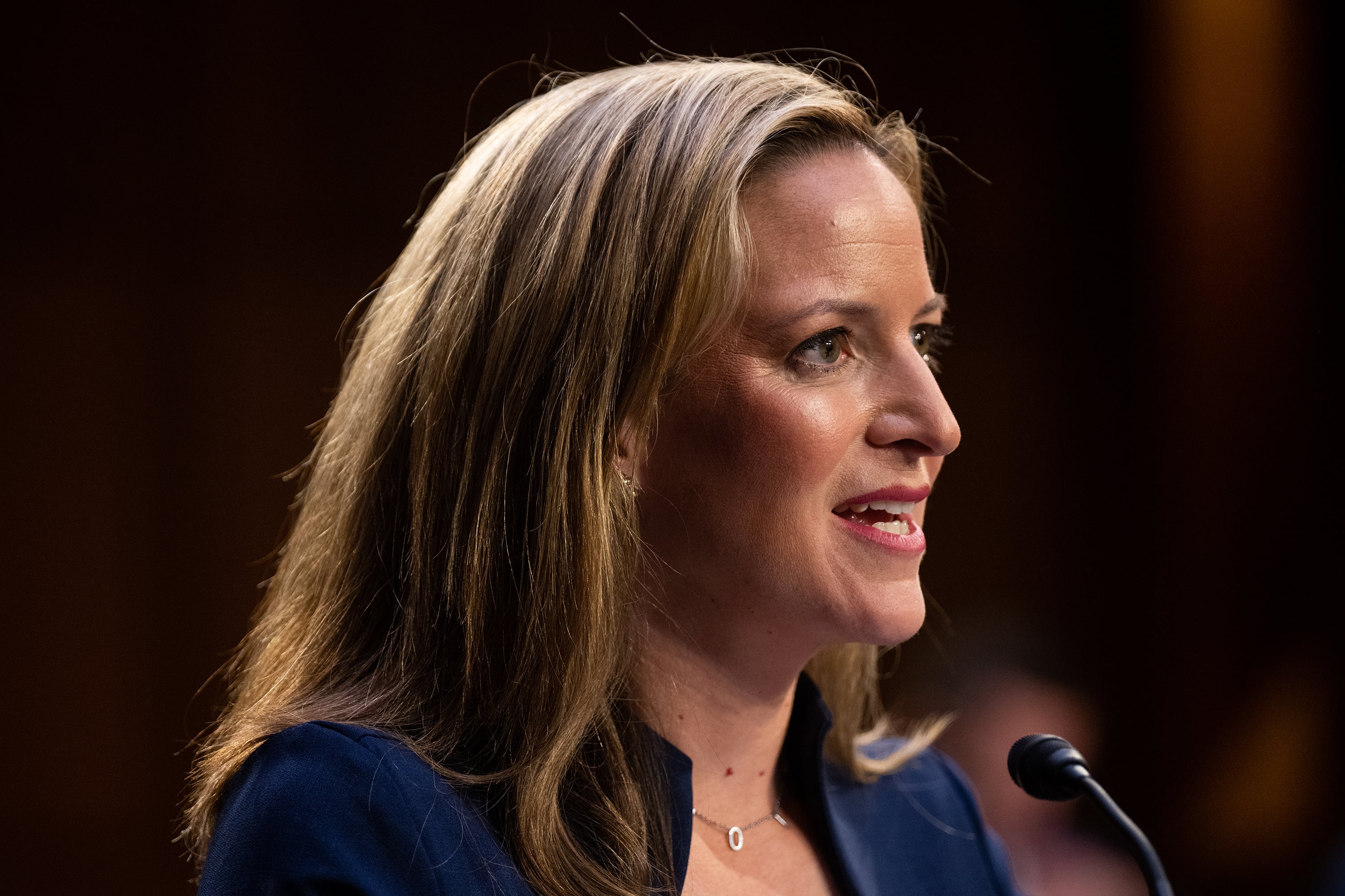 A photograph of a white woman speaking into a microphone.