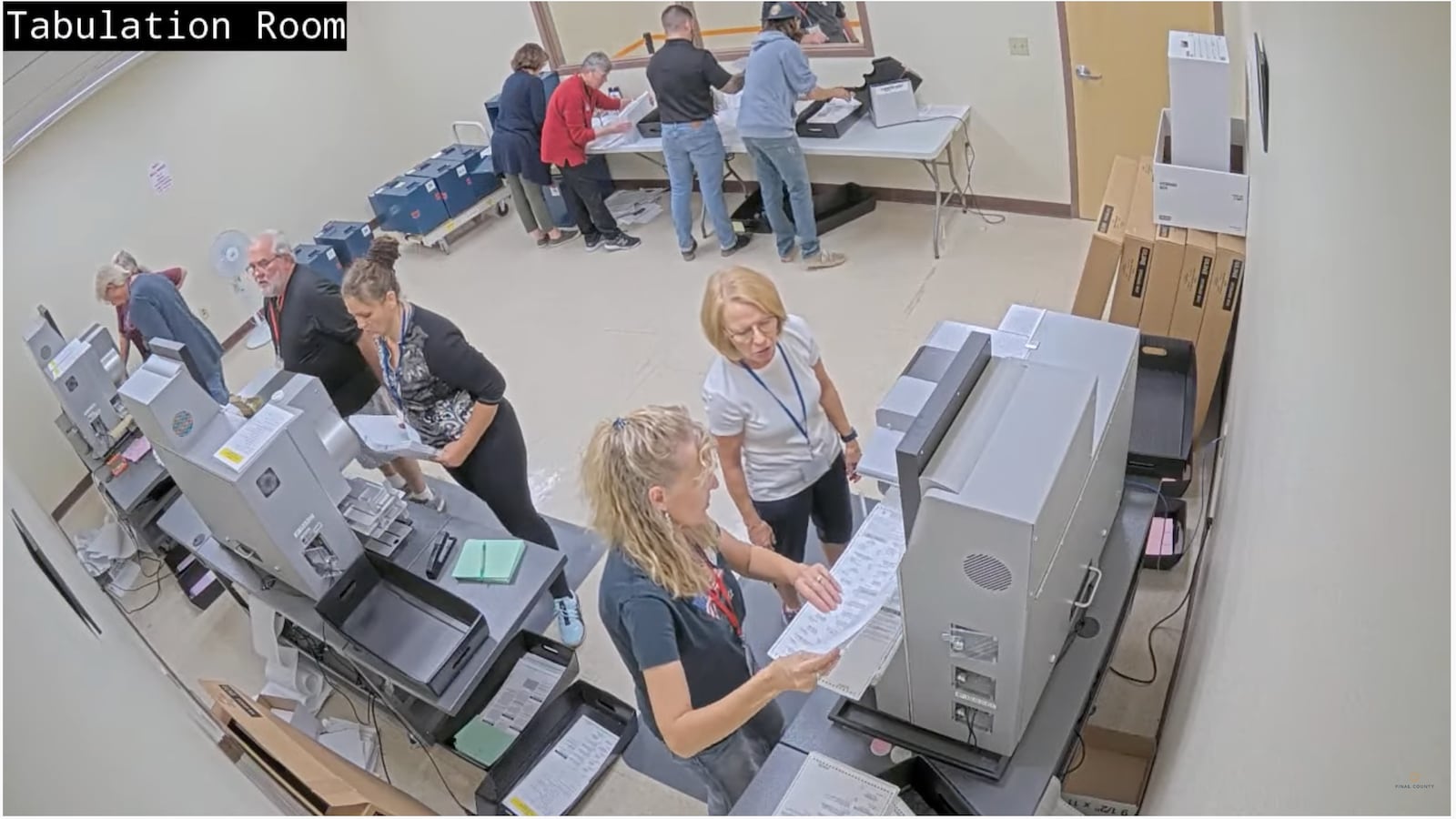 People hold ballots near ballot tabulators in room