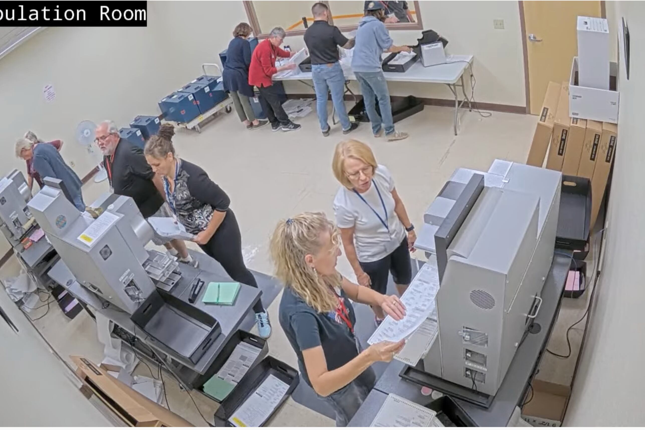 People hold ballots near ballot tabulators in room