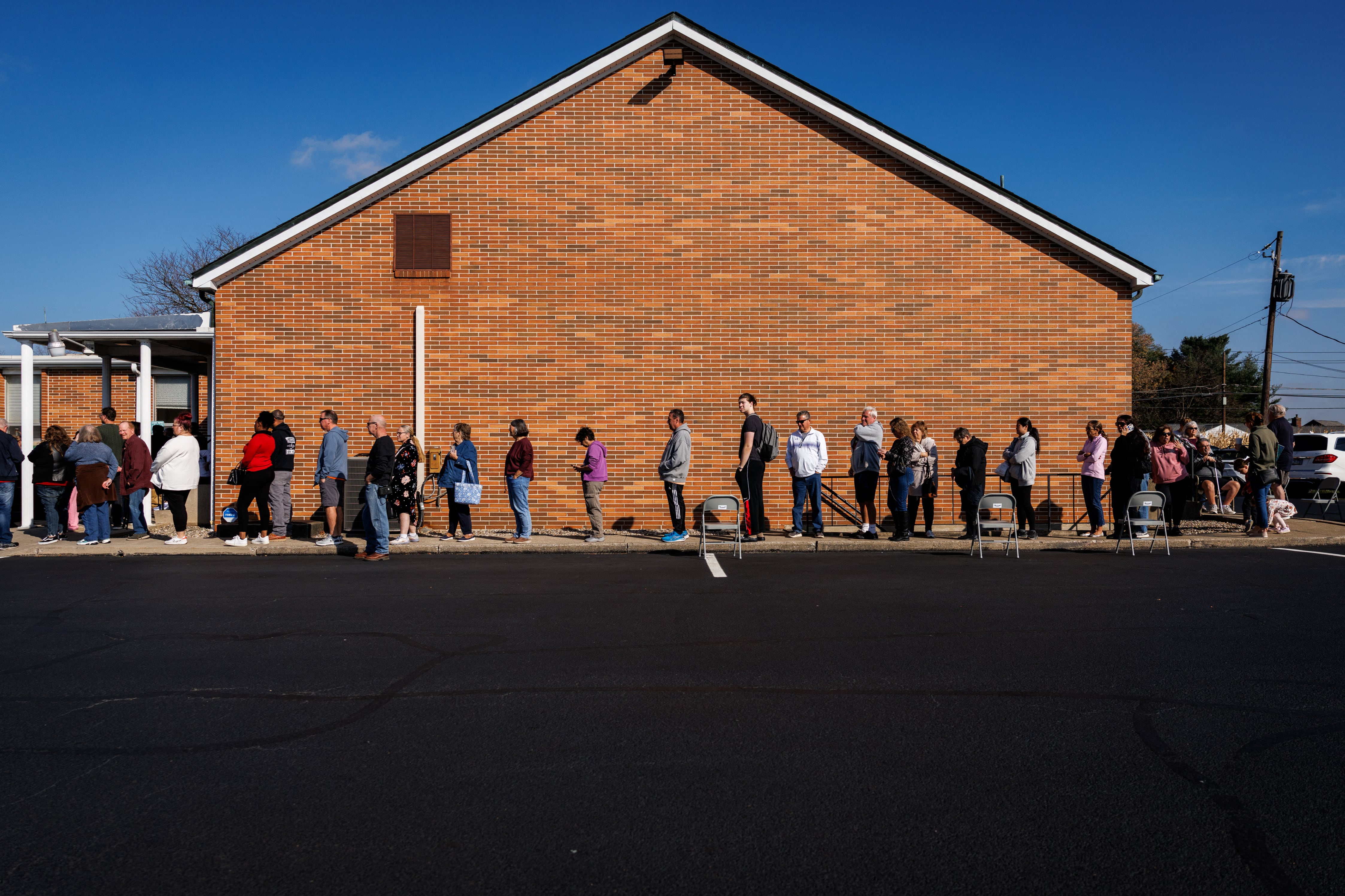 A line of over two dozen people stand in front of a brick building outside.