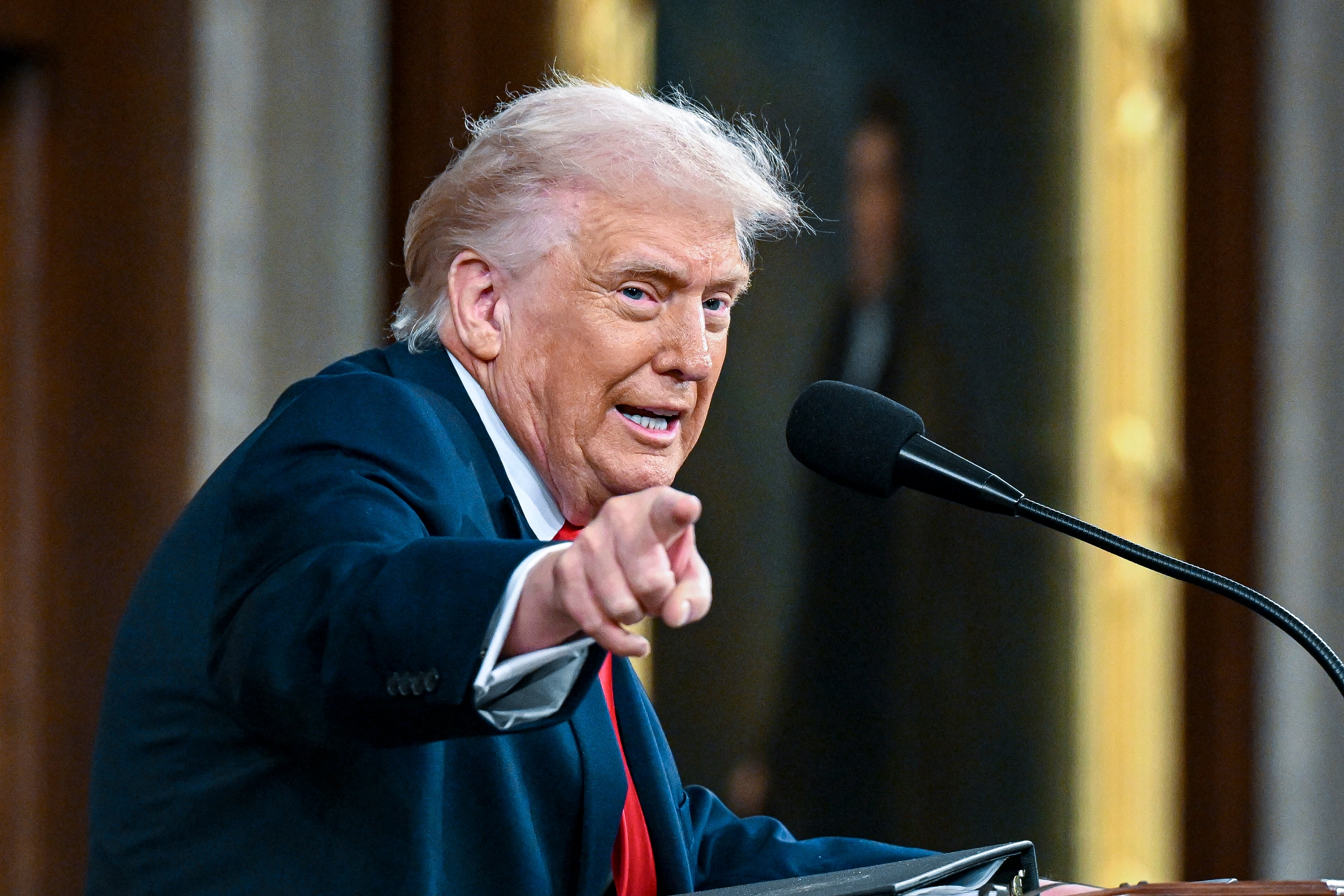 A man in a dark suit jacket points while speaking.