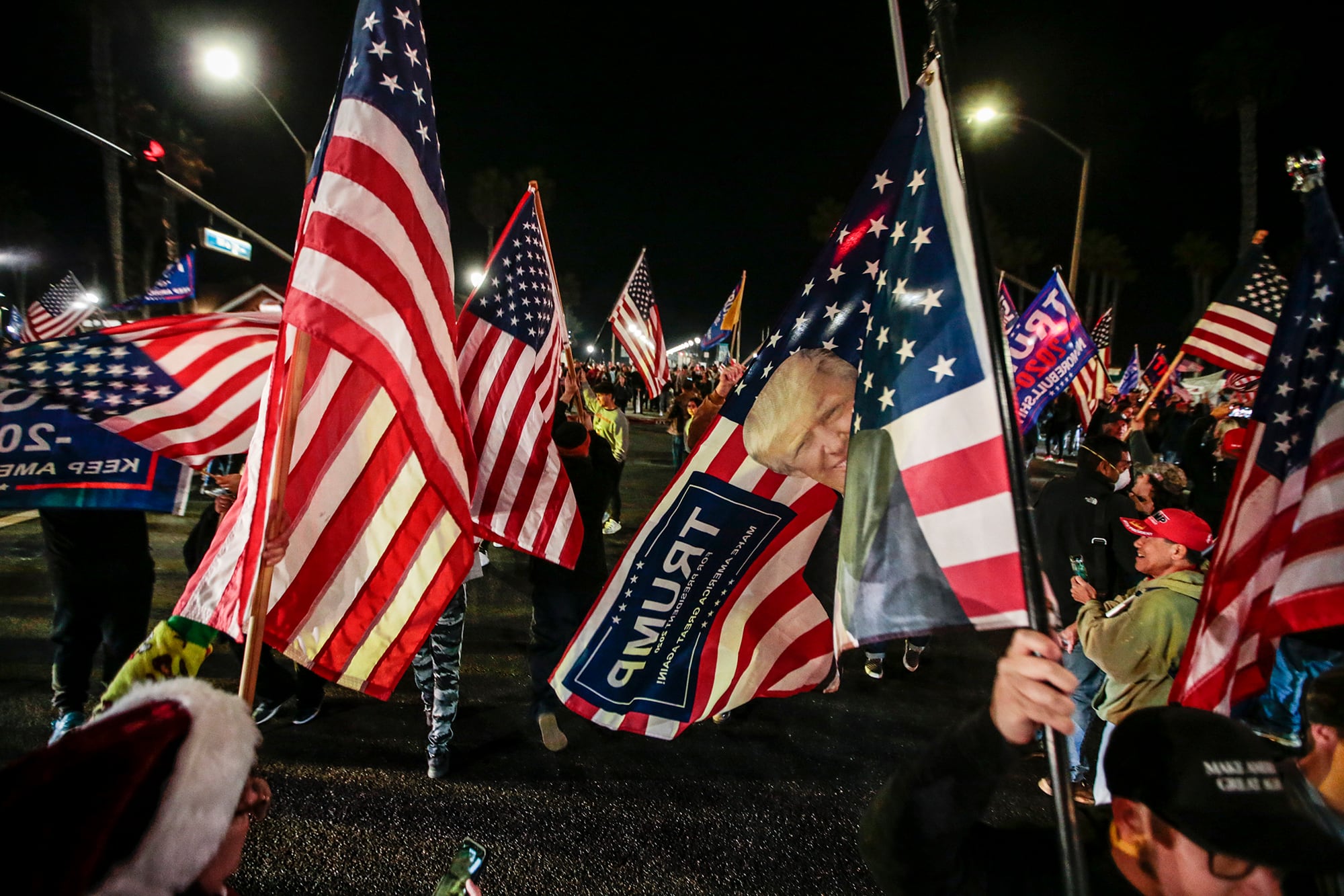 A photograph of a ton of American flags with Trump's face on them at night outside.