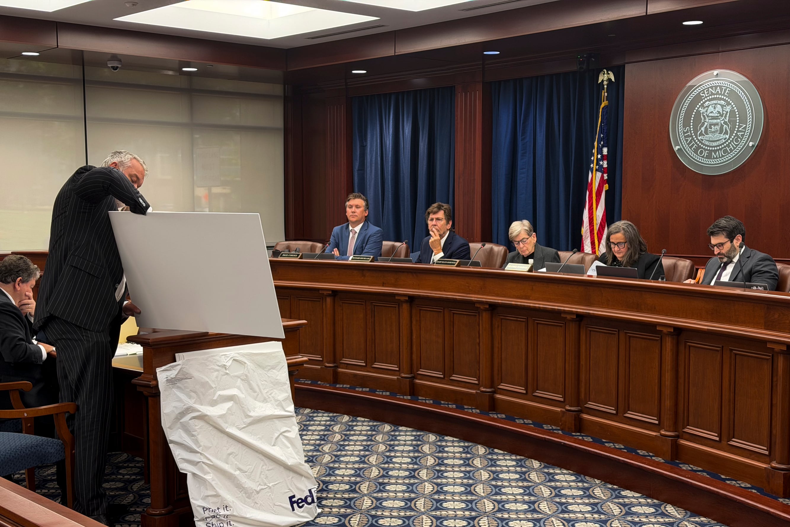 Five people are sitting behind a wooden-colored table.