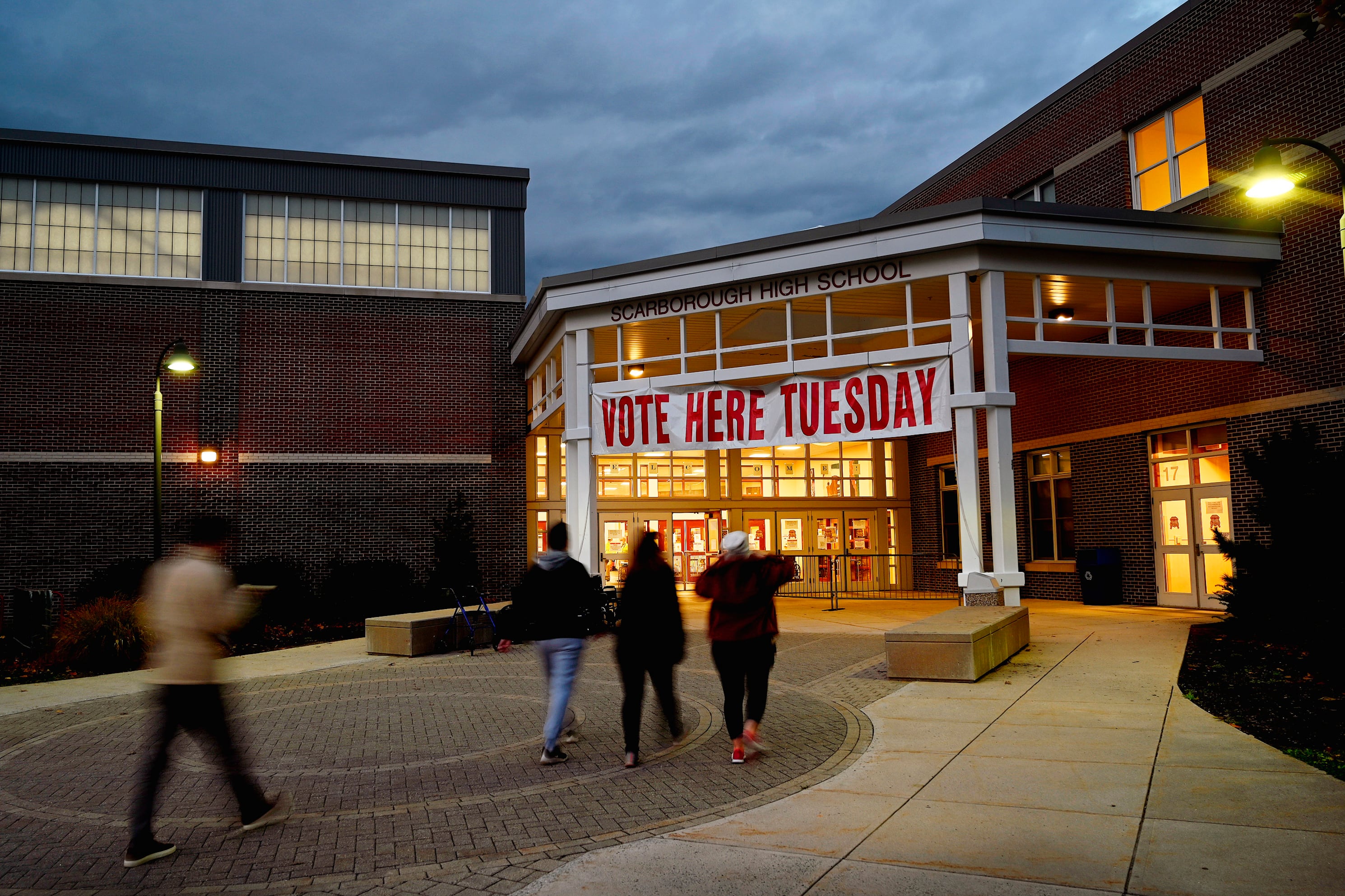 A photograph of the outside of a brown building that has a banner hanging in front of it that reads, " Vote here Tuesday.