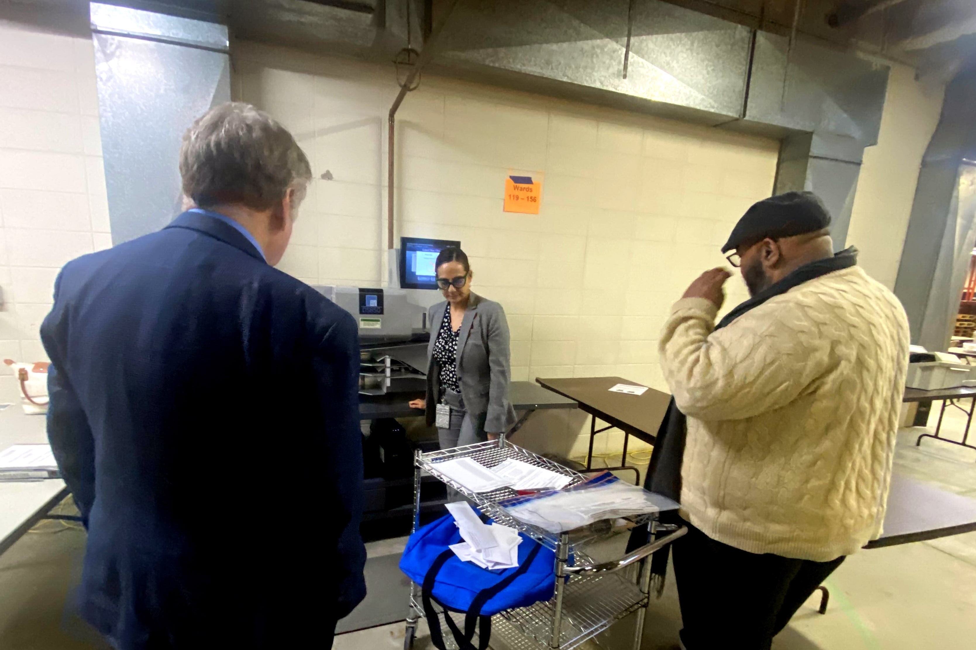 Three people stand around voting materials in a warehouse.