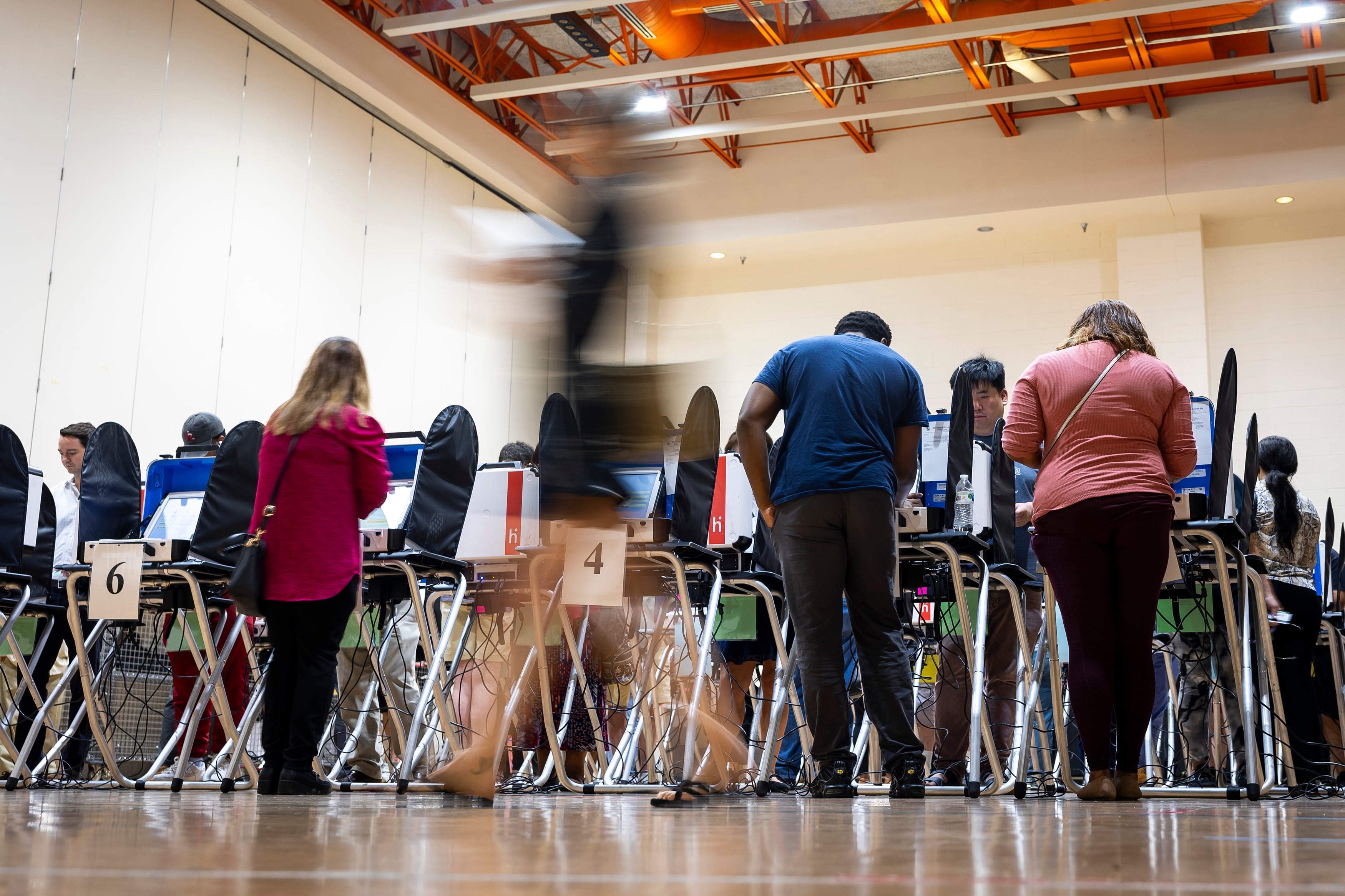 People stand while voting at booths in a room with a high ceiling.