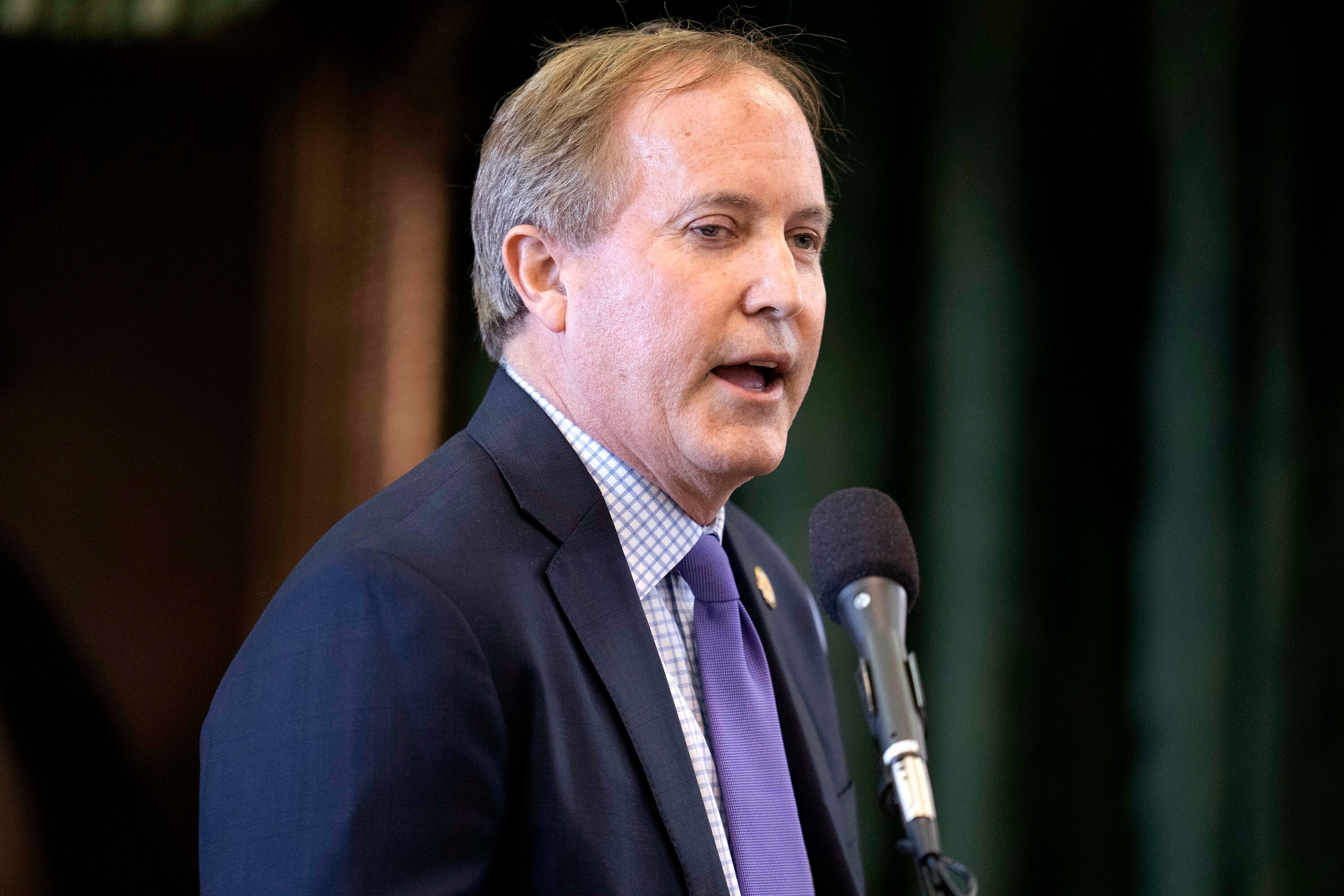 A man in a suit speaks in front of a microphoe