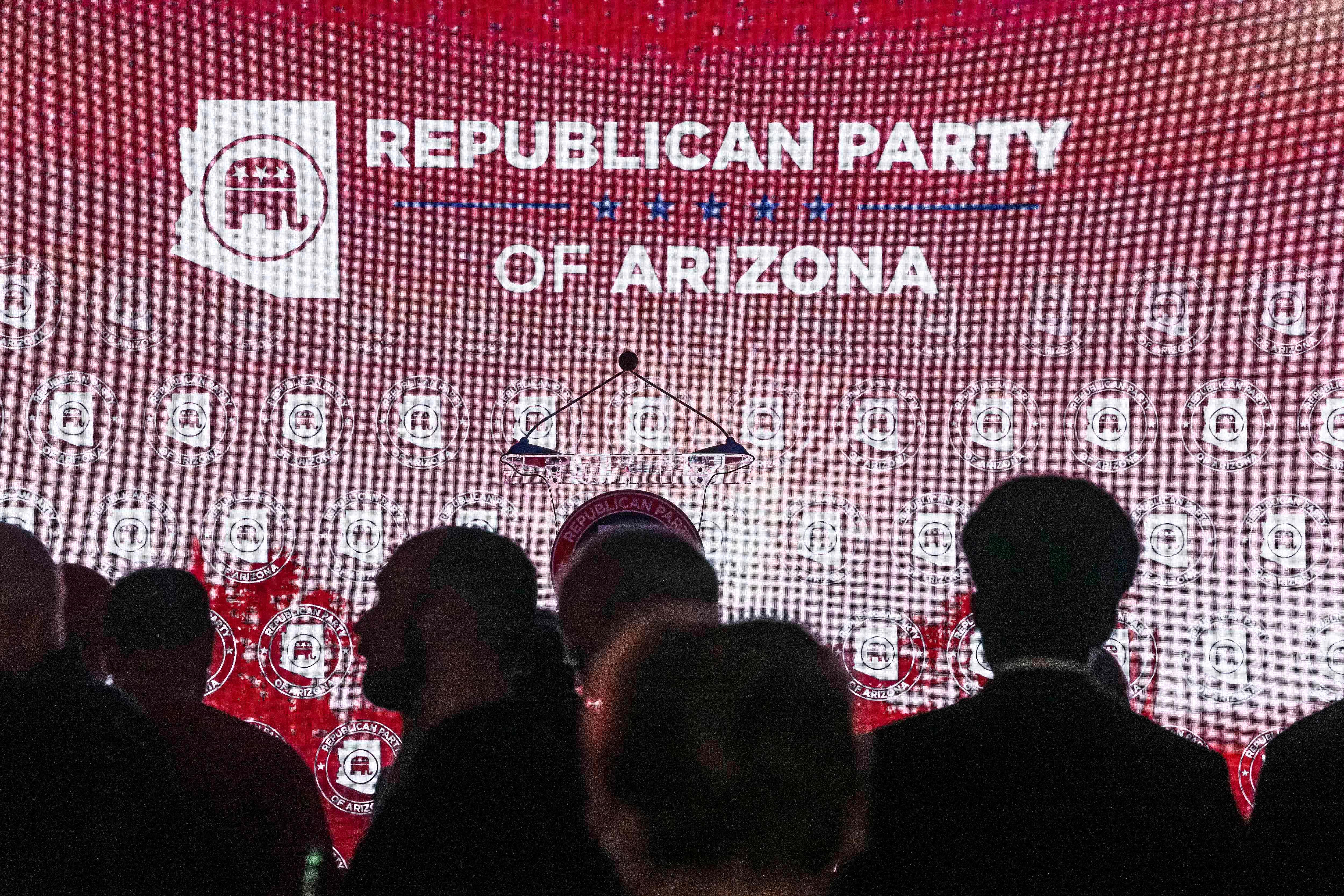 A crowd of people in a dark room in front of a banner reading "Republican Party of Arizona"