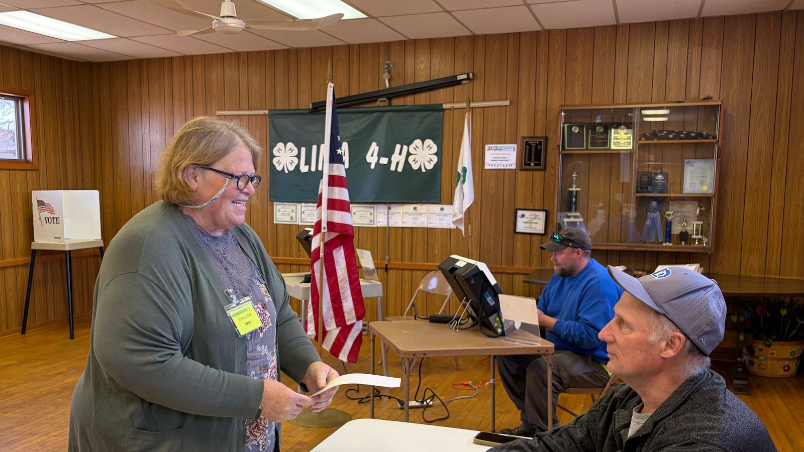 A white woman stands next to two men in a small election room.