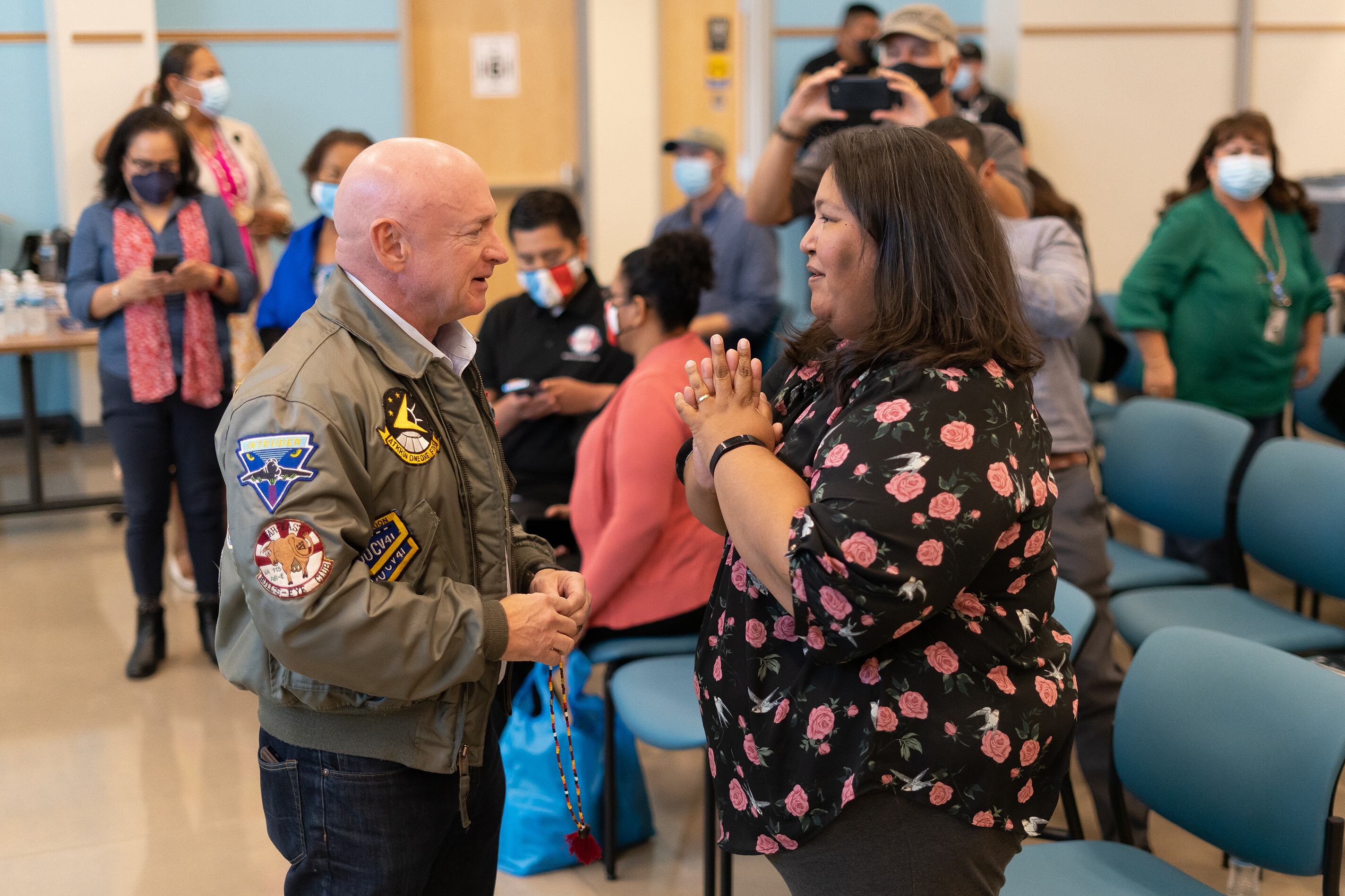A photograph of two adults standing together in a room talking with each other.